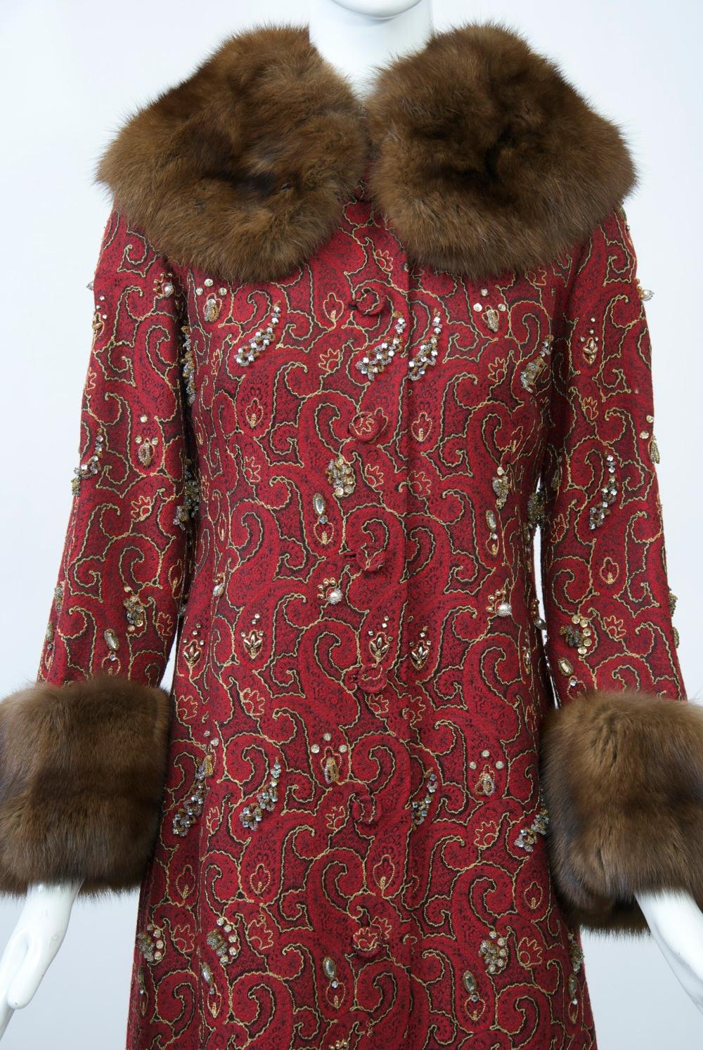 A full-length evening coat crafted out of a lightweight red brocade fabric that is embellished with metallic gold thread outlining the motifs and clusters of beading throughout. Further enhancing this luxurious piece are the sable cuffs and full