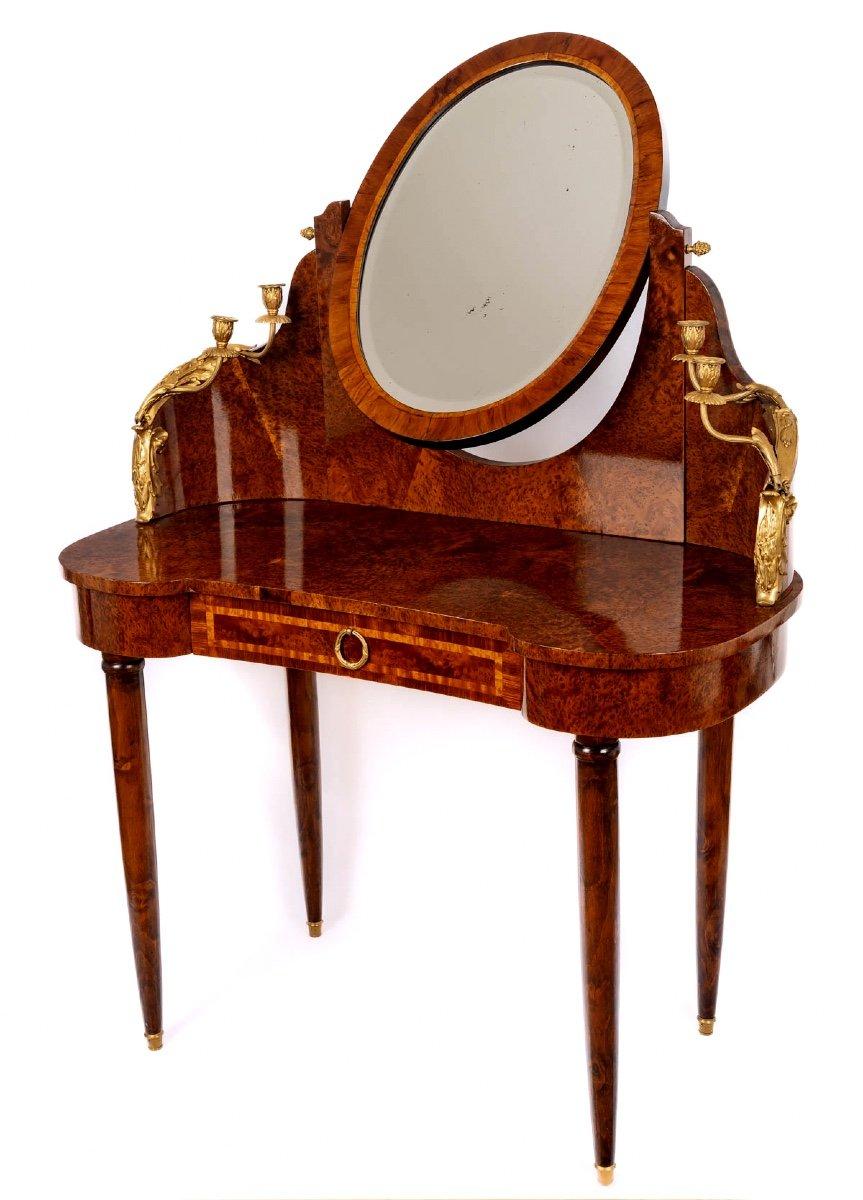 A delightful kidney-shaped dressing table in burr cedar, rosewood and light wood veneer.
It stands on a spindle base enhanced by four ormolu sabots.
It opens with a drawer in the waist and features a reclining psyche with a bevelled mirror, flanked
