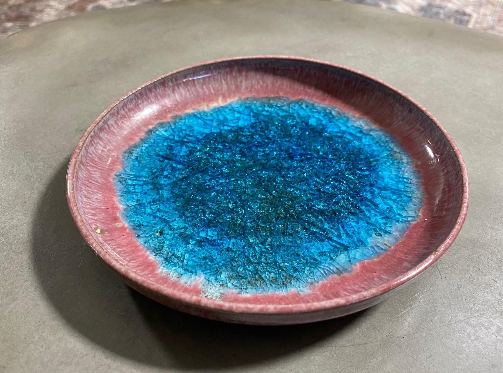 Famed California Mid-Century Modern artist Beatrice Wood signed bowl featuring a unique pink lava glaze and piercing blue crackle glass in the center of the bowl/dish. The sumptuous glaze runs down the backsides and gathers in areas underneath.
