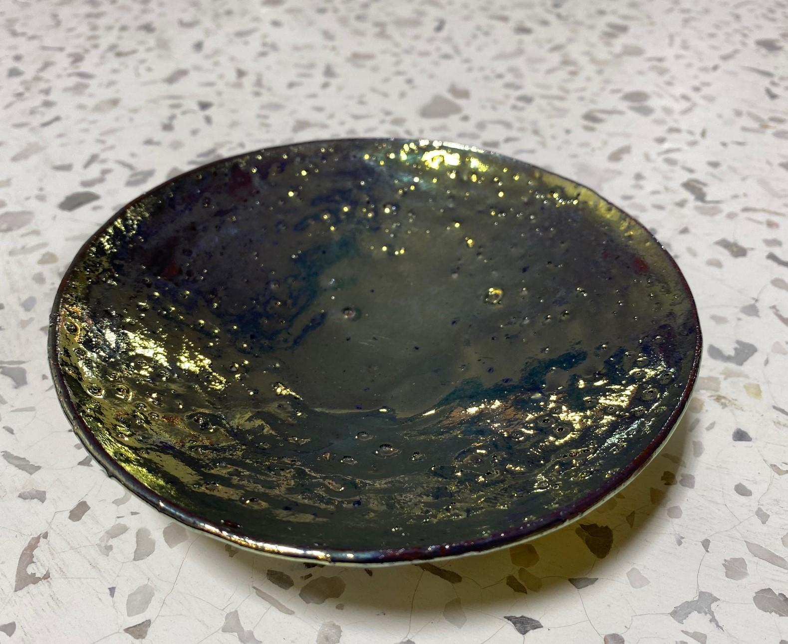 A wonderfully designed and sumptuously glazed work by famed American/California ceramicist Beatrice Wood featuring her highly coveted, and somewhat rare volcanic iridescent gold luster (lustre) glaze. This small bowl/plate has tons of character and