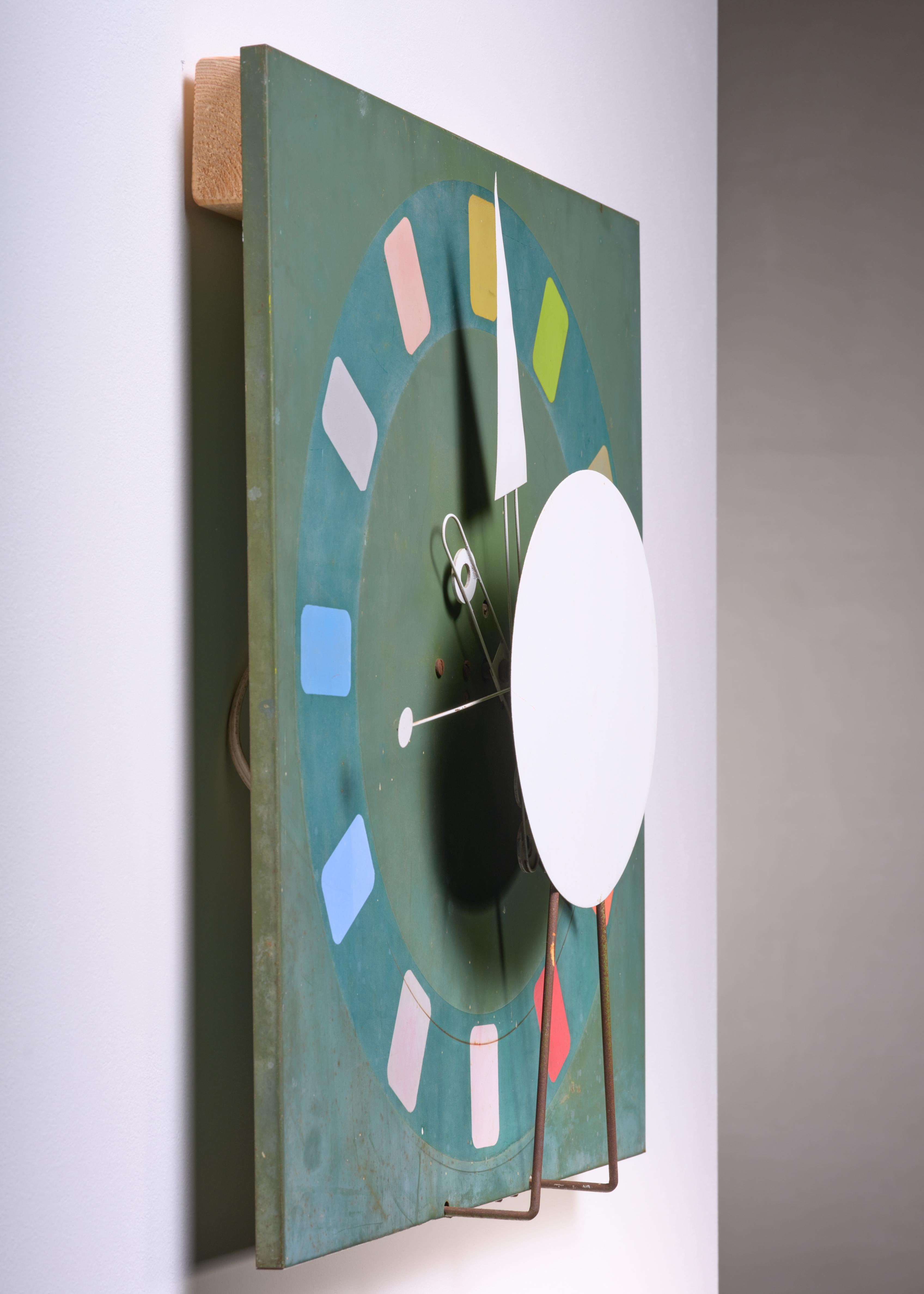 A large mid-century American wall clock in working condition.

Metal back plate with beautiful 1950s colour blocking signing on the hours.

Colours varying from, soft white and pink to blue, yellow green and red in a Modernist colour spectrum.