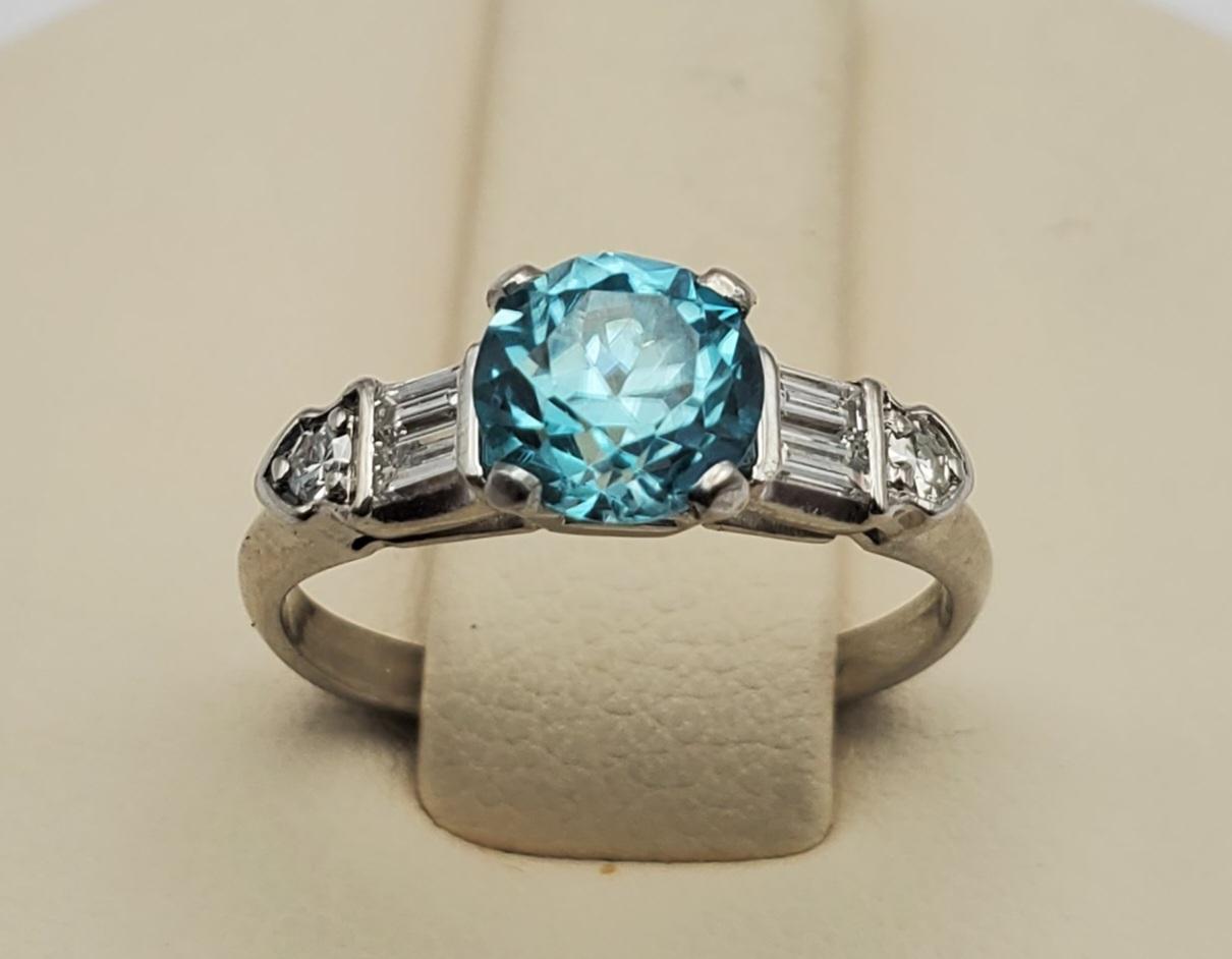 Beautiful and unusual blue zircon and diamond ring. The ring features a 1.61ct round blue zircon that is eye clean and vibrant in color. The mounting contains four baguette and two round brilliant cut diamonds and with a total weight of 0.25cts. The