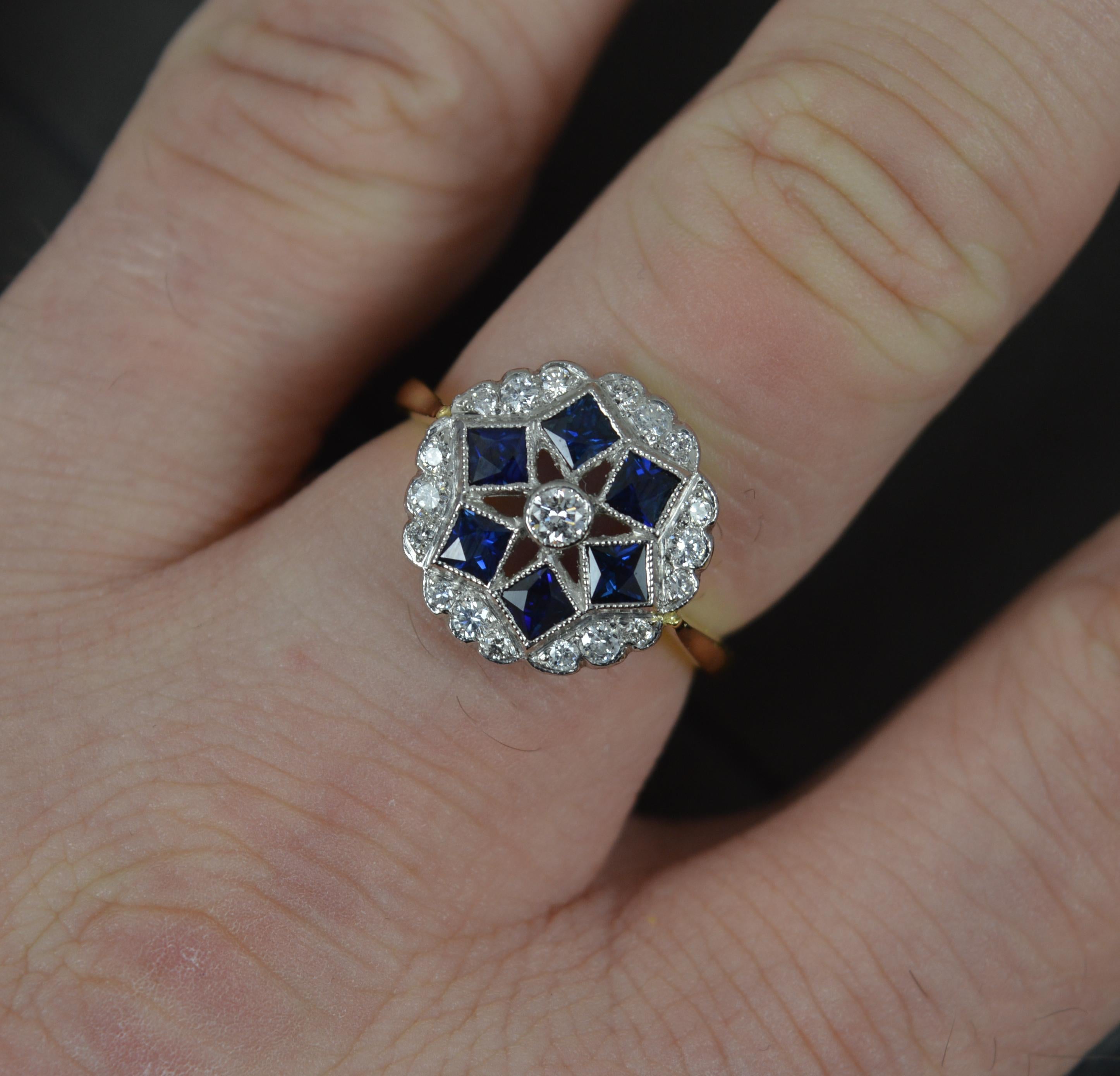 A superb contemporary cluster panel ring.
Solid 18 carat yellow gold shank with white gold head setting.
A circular panel set with many round brilliant cut diamonds and six French cut sapphires into a pierced head. 
14mm x 14mm cluster head.