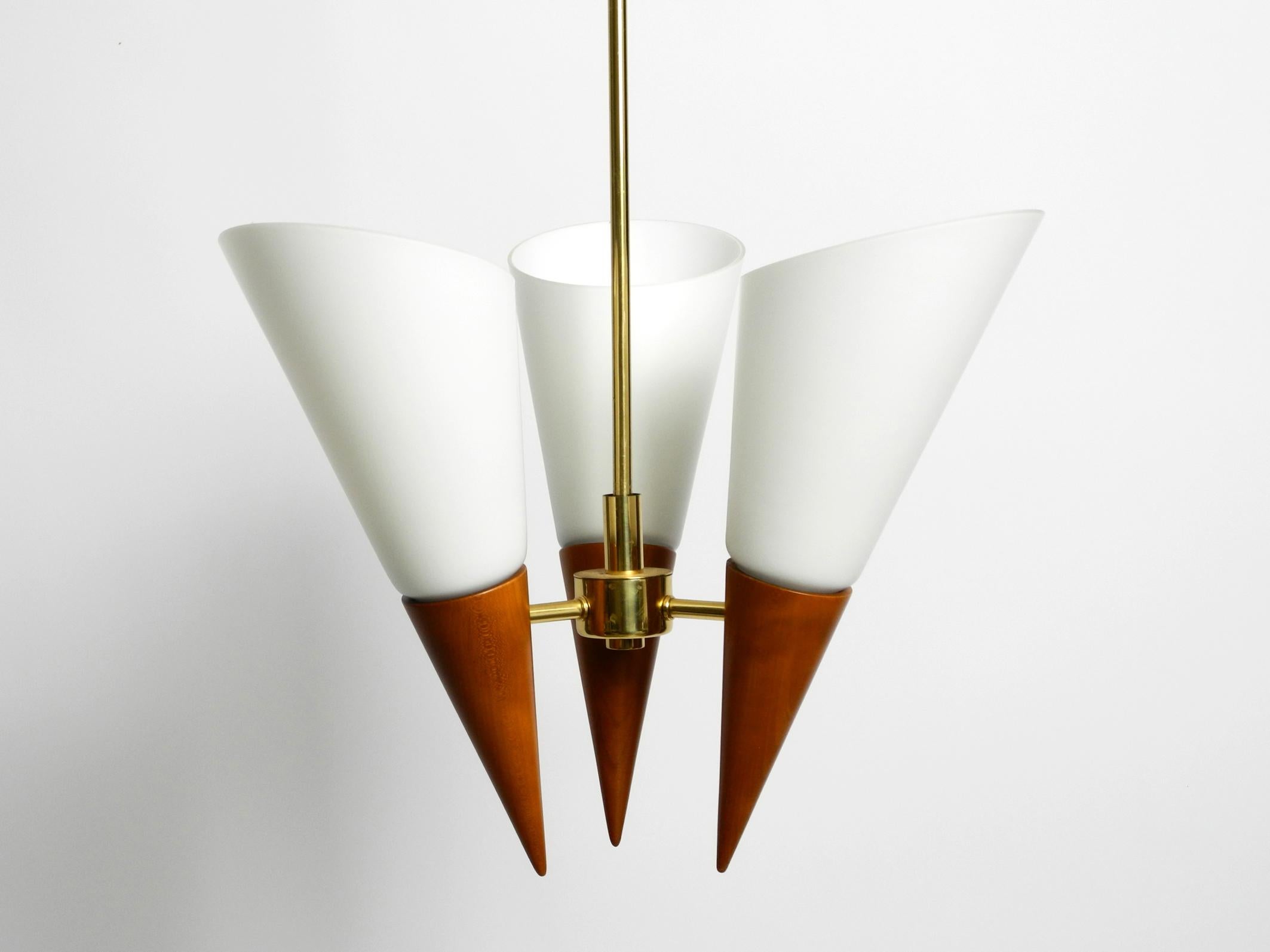 Schöne Deckenlampe aus den 1960er Jahren. Großartiges elegantes Design. Hergestellt in Deutschland.
Rahmen, Stange und Baldachin aus Messing.
Die Zapfen sind aus Kirschholz gefertigt. Mit großen, dicken Glasschirmen.
Eine sehr hochwertige Lampe für