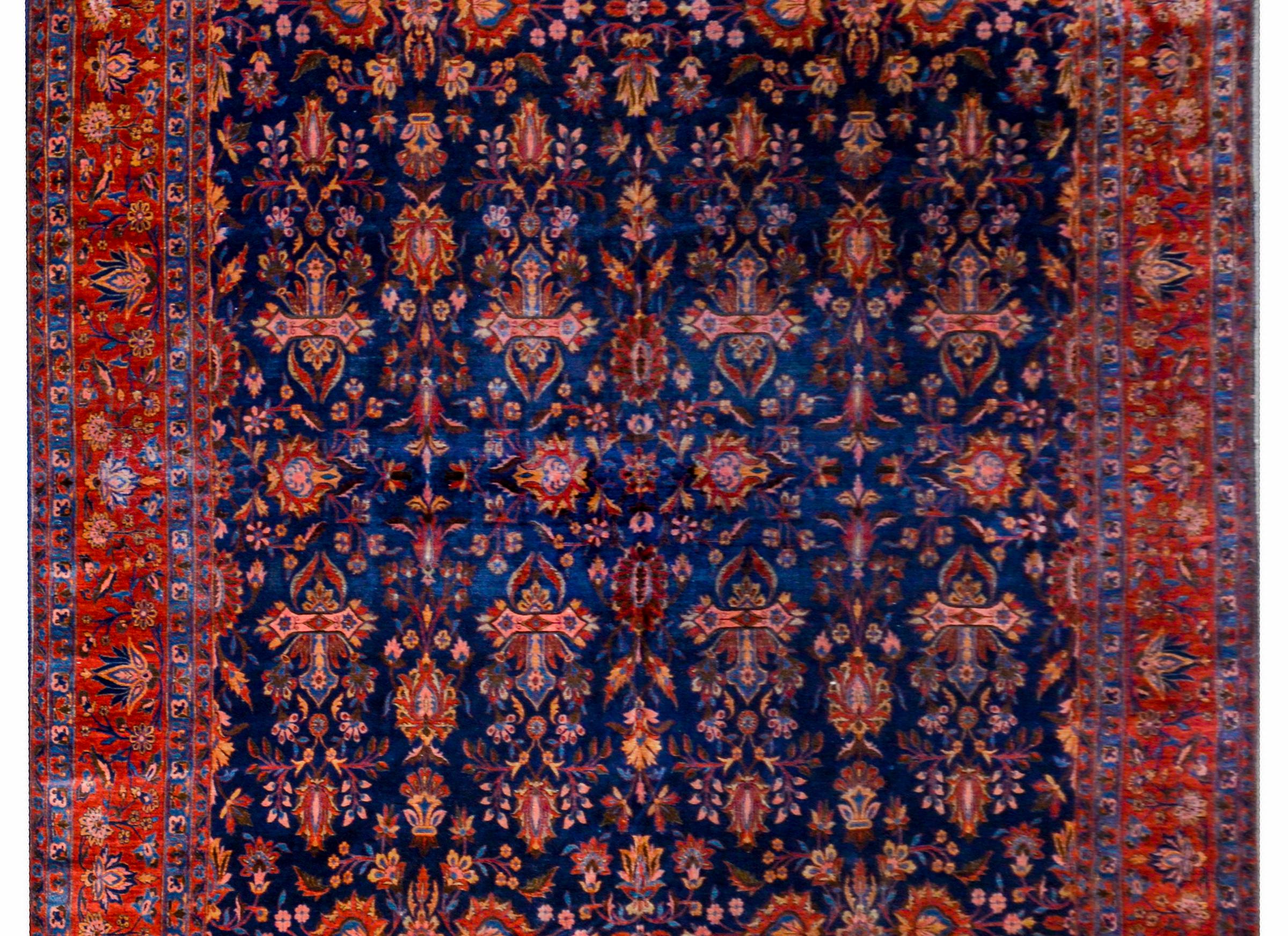 A beautiful 19th century antique Kashan rug with a central field containing myriad mirrored floral pattern woven in crimson, light and dark indigo, and gold on a dark indigo background surrounded by a wide central floral and vine stripe on a crimson