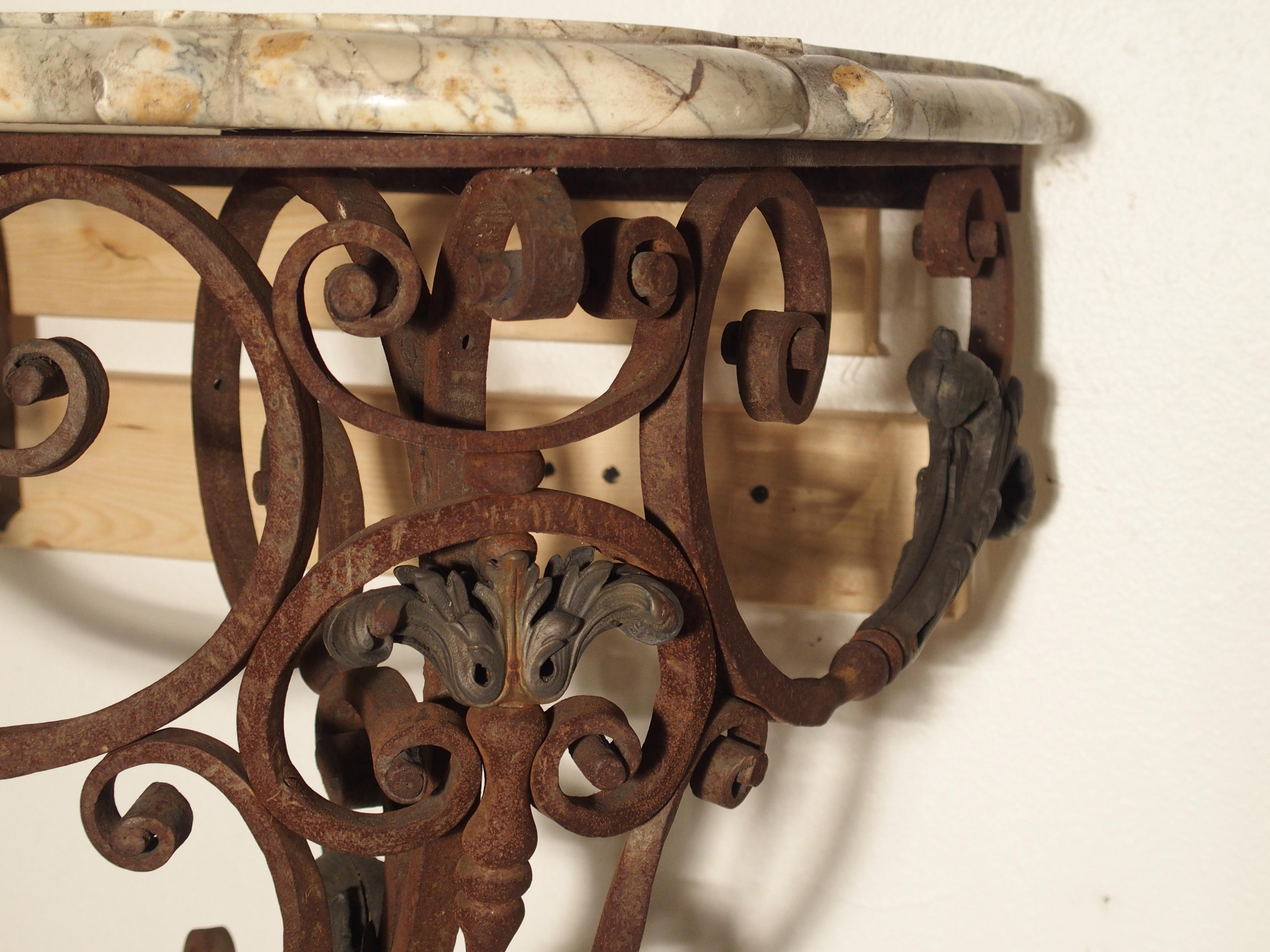 This unusual scrolling wrought iron and bronze console table has a light colored variegated, shaped marble top. The handsome marble top is original to the piece and is cut in a thick manner, with rounded corners and shaped sides. The consoles