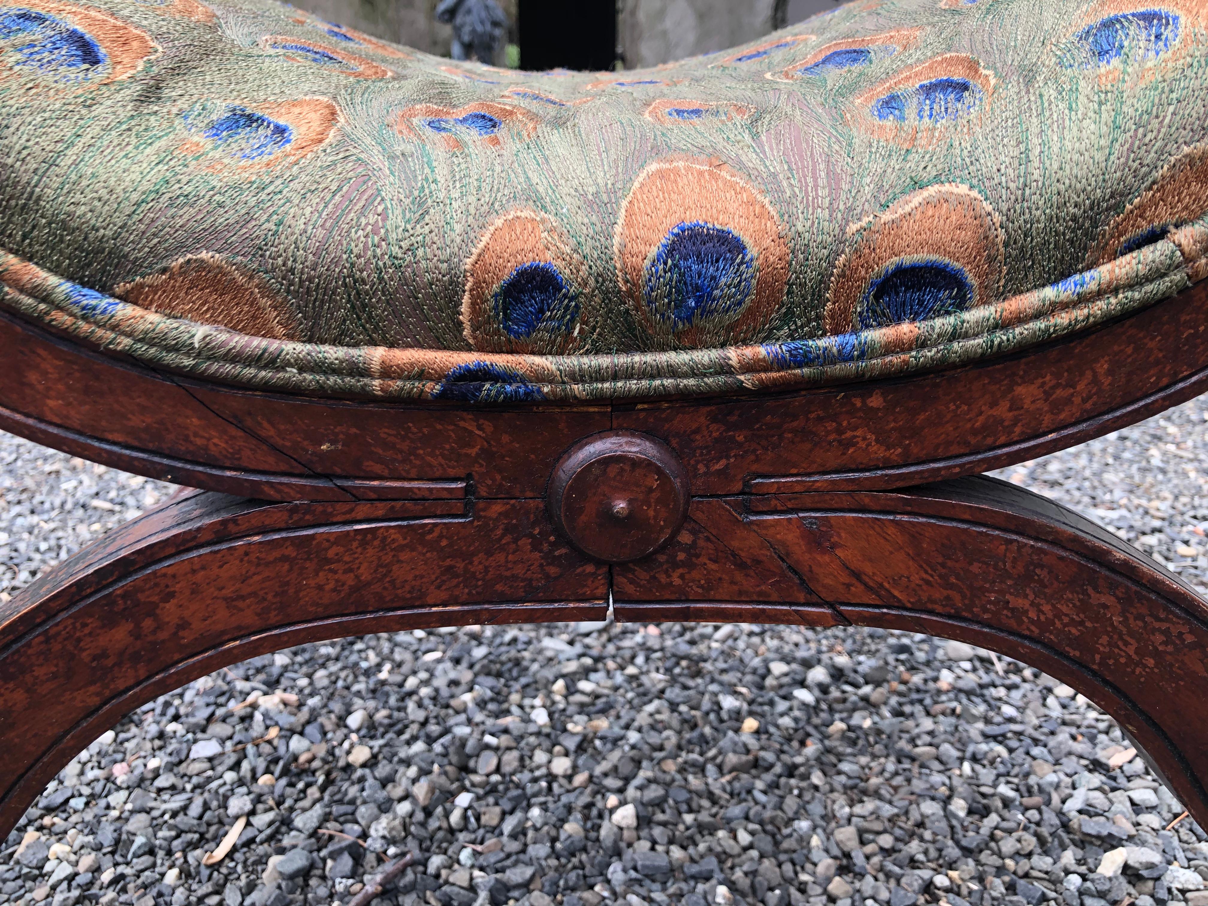 A beautiful 19th century Curule bench from Italy upholstered in a green, blue and gold peacock patterned silk having lion head finials and paw feet. The wood has great patina.