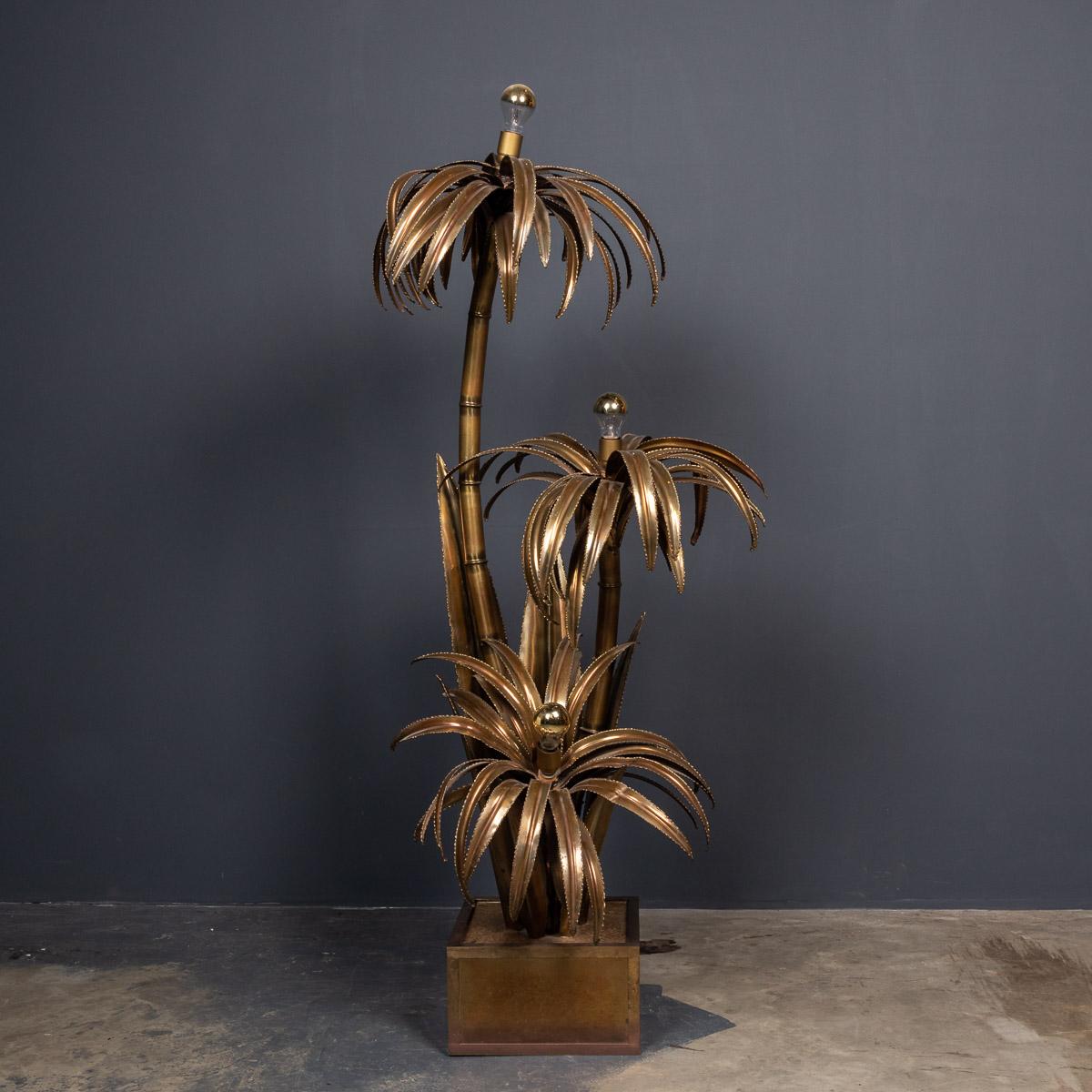 A large Maison Jansen palm tree floor lamp in Hollywood regency style. The golden, copper coloured brass leafs of the palm reflect a warm atmosphere in the room. The palm rests on a very stylish square brass foot lined with a soft brown velvet, the