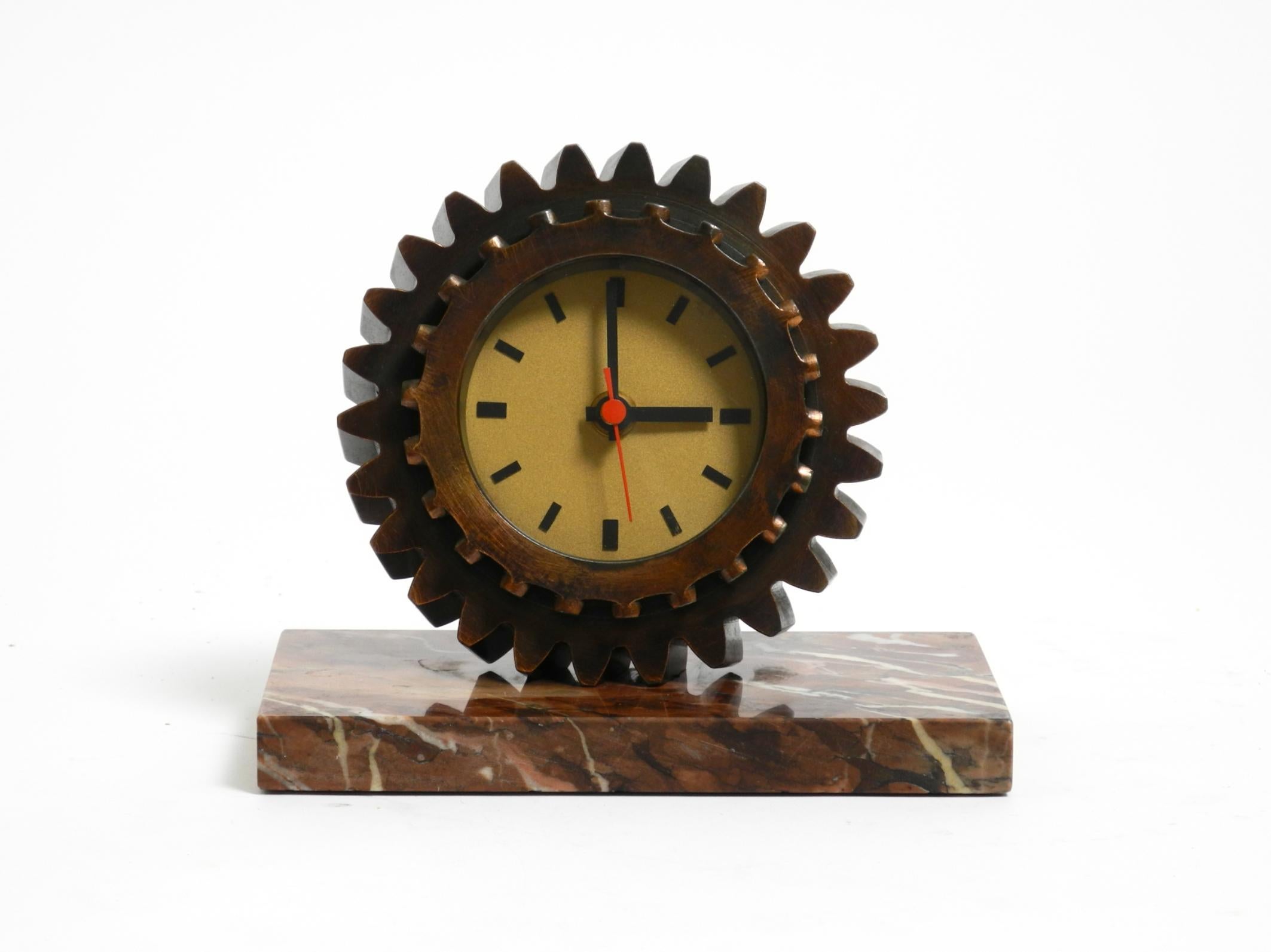 Un precioso y pesado reloj de sobremesa de los años 70, fabricado con un engranaje doble de hierro chapado en cobre.
La base, igualmente pesada, es de mármol. En total pesa aproximadamente 5 kg.
La esfera del reloj está detrás de un cristal.
El