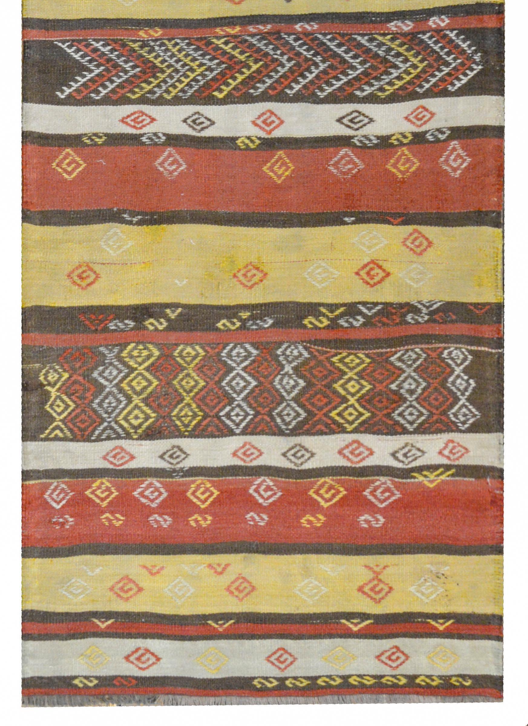 A beautiful vintage Anatolian Turkish Kilim runner with a crimson, gold, brown, and white striped pattern with embroidered geometric patterns with chevrons and stripes.