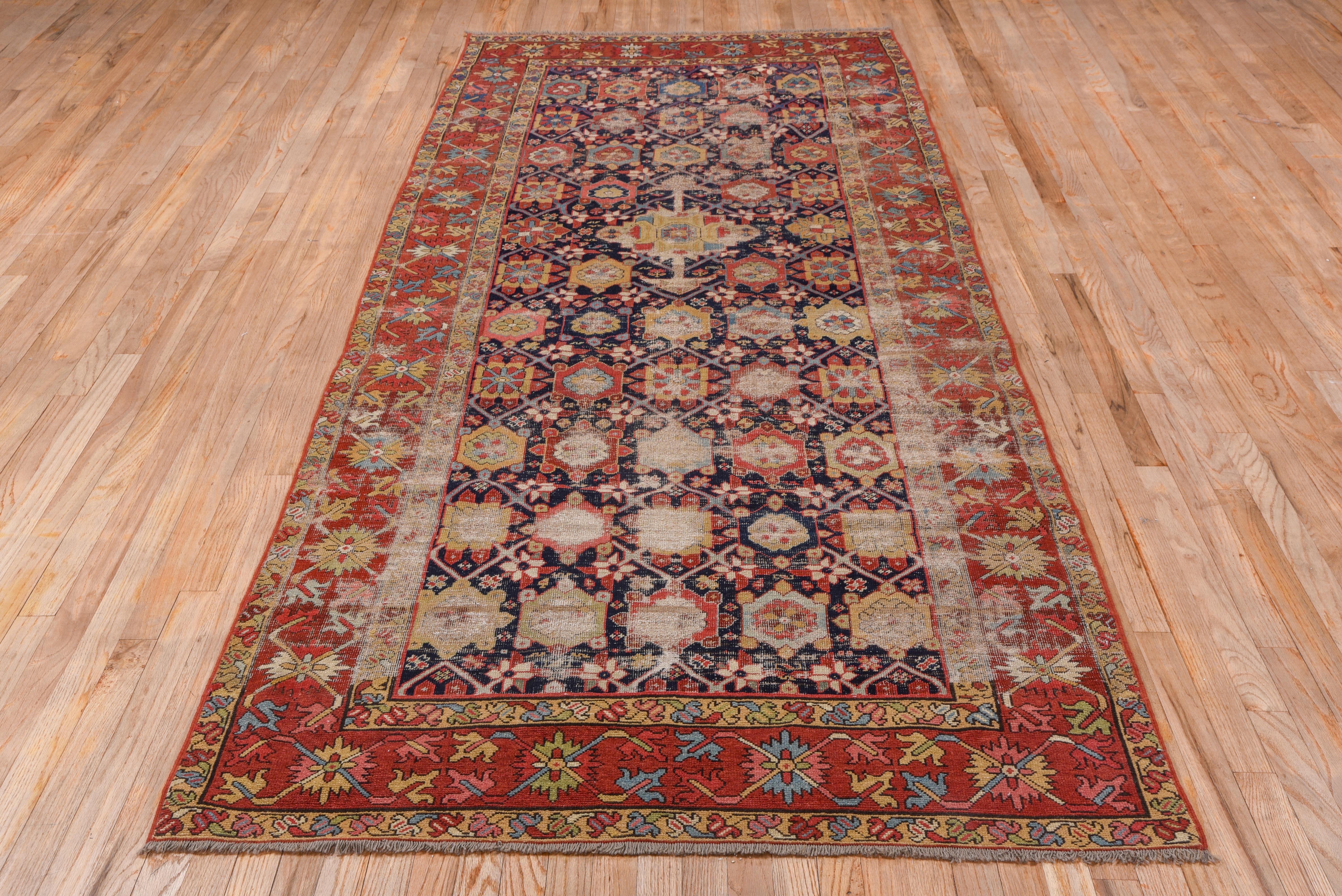 This south Caucasian long rug retains the characteristic dark blue field with its geometric rendering of the Persian Mina Khani rosette trellis design, set within a red crab palmette border.