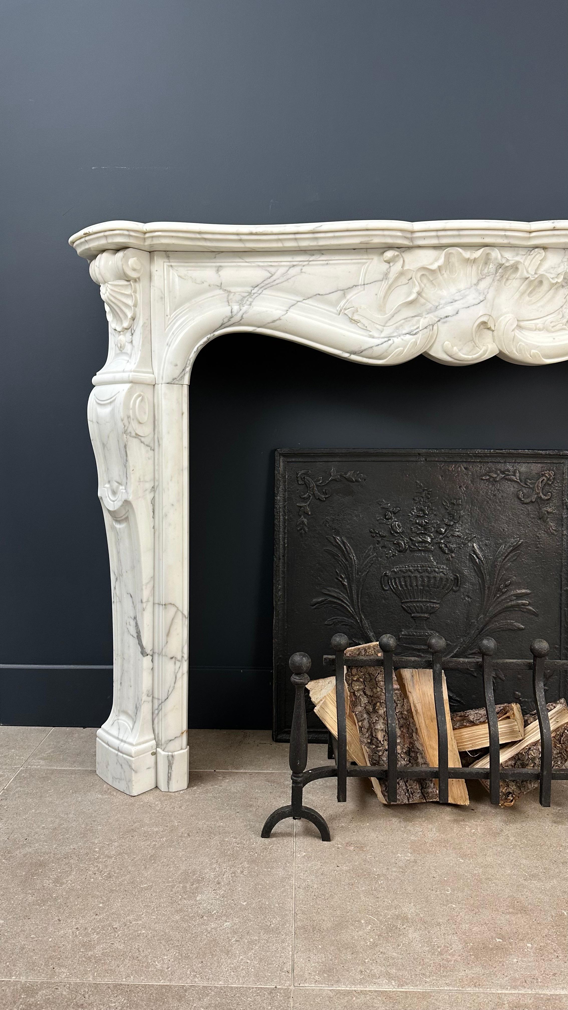 Indulge in the timeless charm of this exquisite antique front fireplace. Crafted in the opulent Rococo style, this fireplace stands as a testament to the artistry of a bygone era. Meticulously carved from a stunning veined white marble, every detail