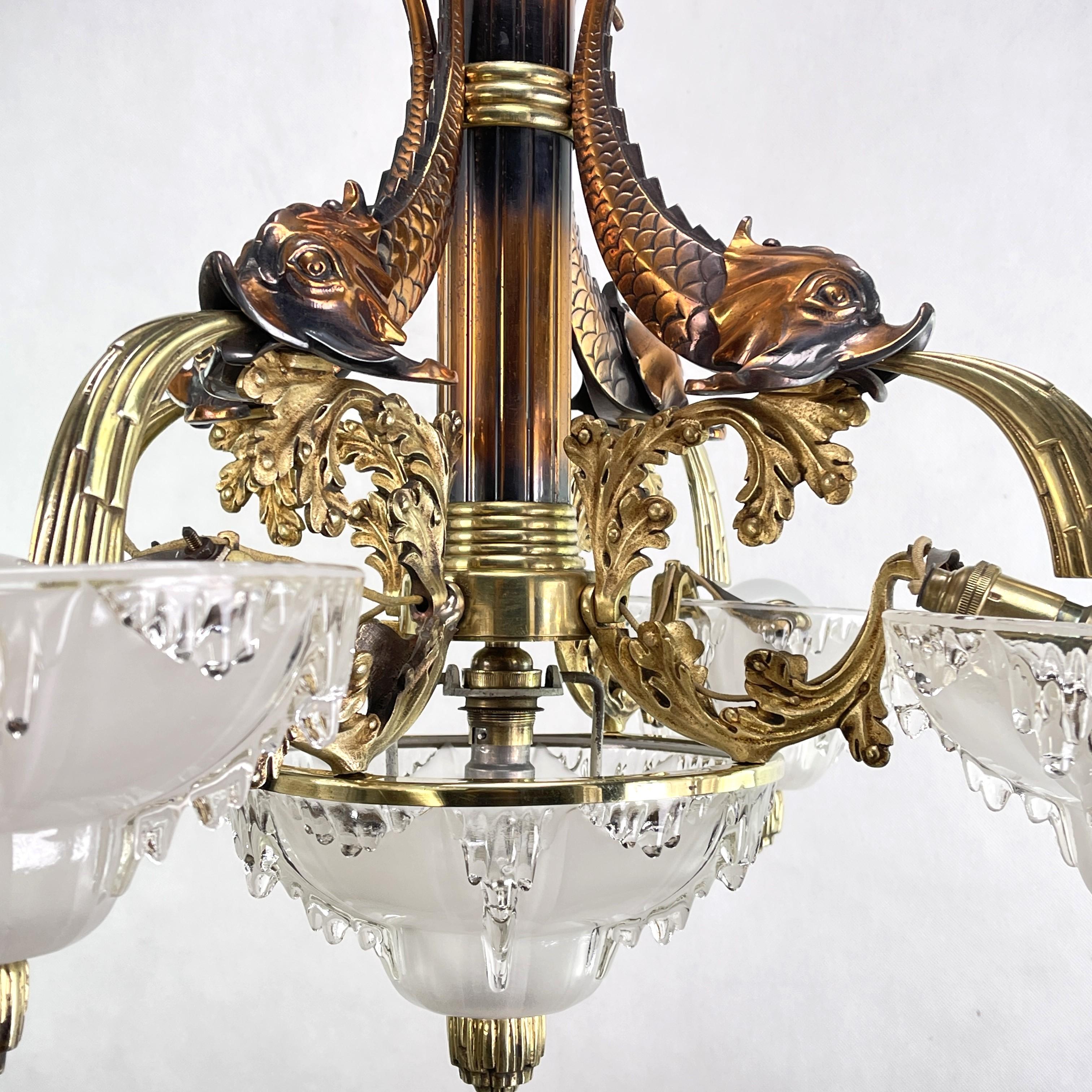 Cette suspension originale de PETITOT impressionne par son design Art déco. La lampe est signée M.P. et donne une lumière très agréable. Elle est composée de cinq abat-jour en verre épais et de quatre poissons en bronze qui jettent de l'eau.

Ce