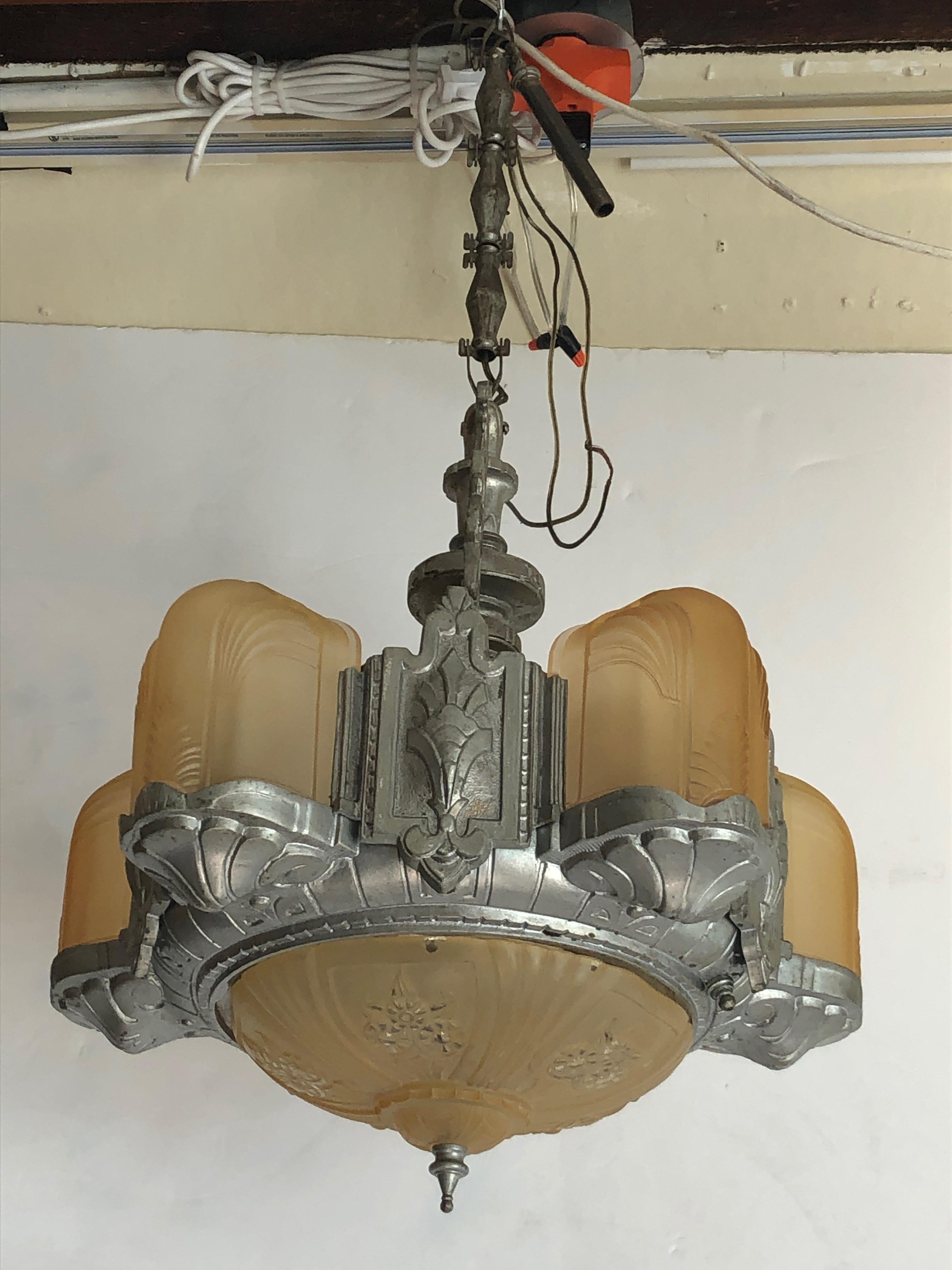 A beautiful period Art Deco light fixture having 5 gold frosted glass shades around the periphery and an ornate matching bowl of glass at the bottom. Decorative pewter colored metal creates the body of the chandelier. Original ornate chain and