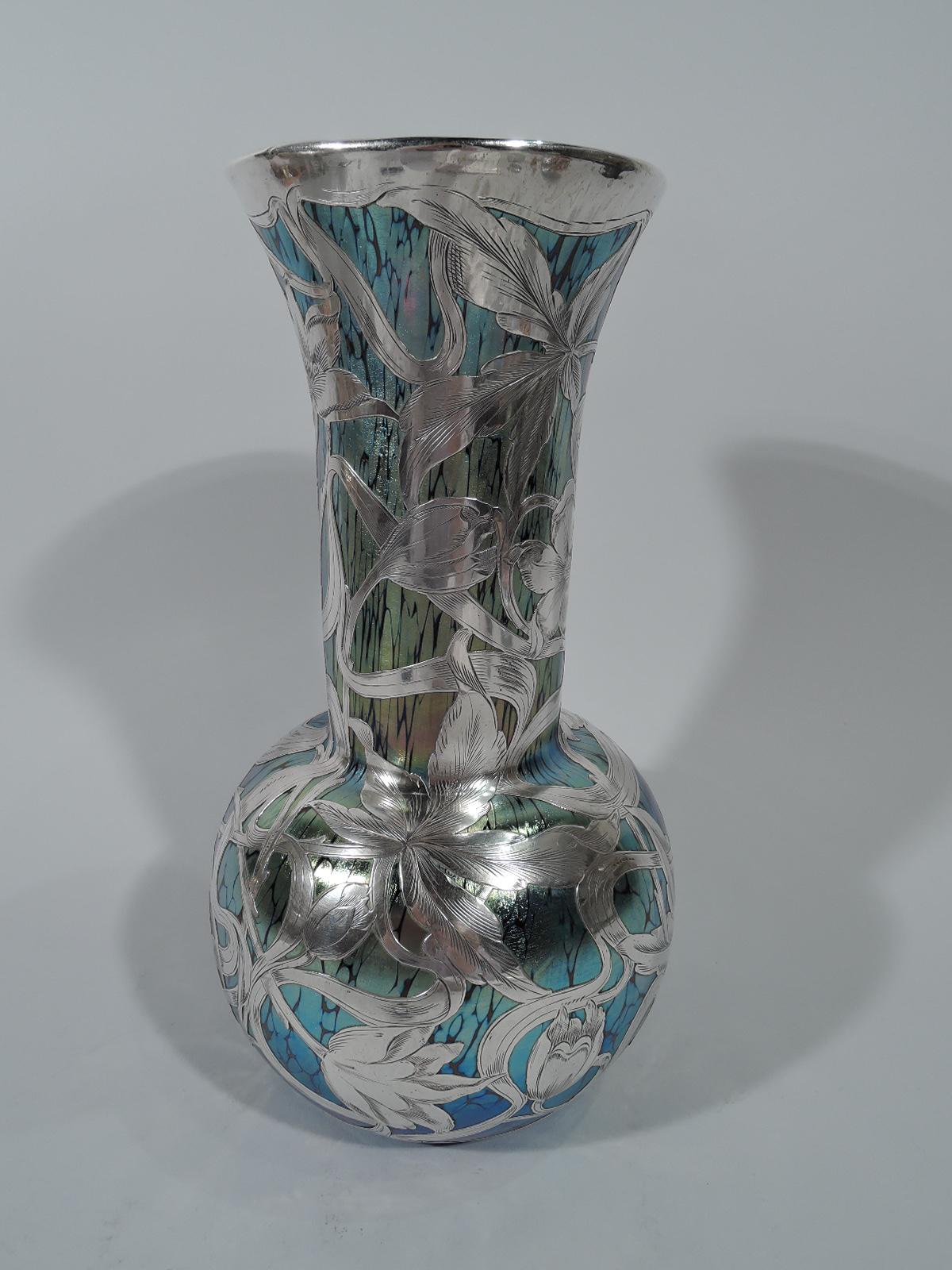Art Nouveau glass vase with engraved silver overlay by historic Czech maker Loetz. Globular with cylindrical neck and flared rim. Glass is veined iridescent blue. Fluid and dynamic overlay in form of naturalistic blooms with interlacing stems.
