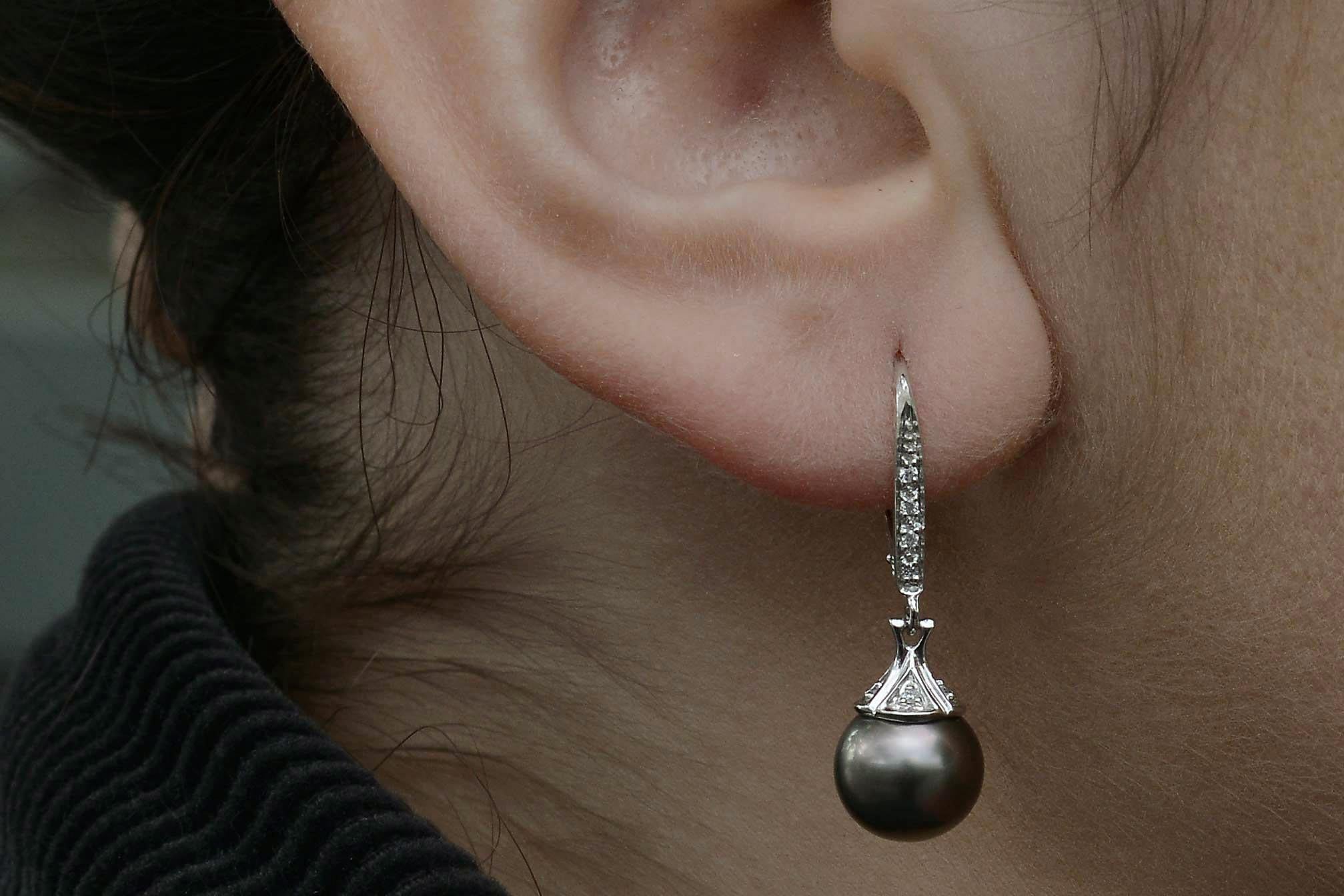 A pair of beautiful black Tahitian pearl drop earrings, diamonds dangle seductively from the ear. A lustrous dark silvery grayish black of a substantial 9mm diameter suspended from a studded bar and held with pave' diamond caps that evoke the chic,