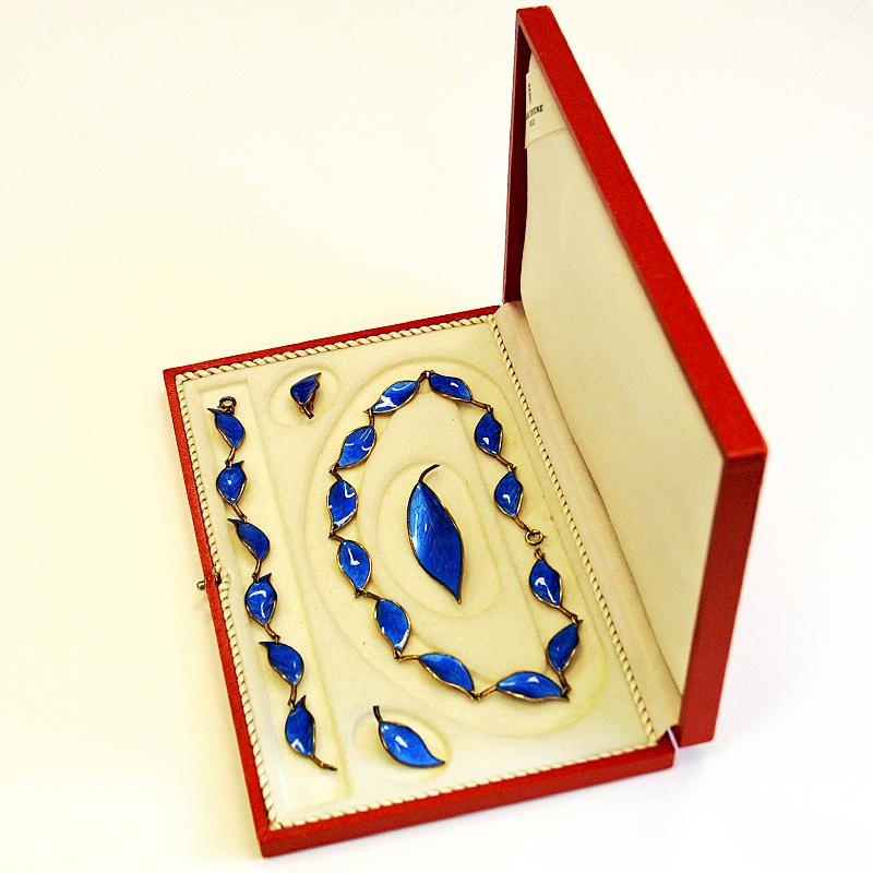 Explosive deep blue Jewelry set of gold plated silver by mid-century designer Willy Winnæss for David Andersen in 1966. This vintage set consists of a clear blue enamelled necklace, a brooch, a bracelet and a pair of clip earrings in the original