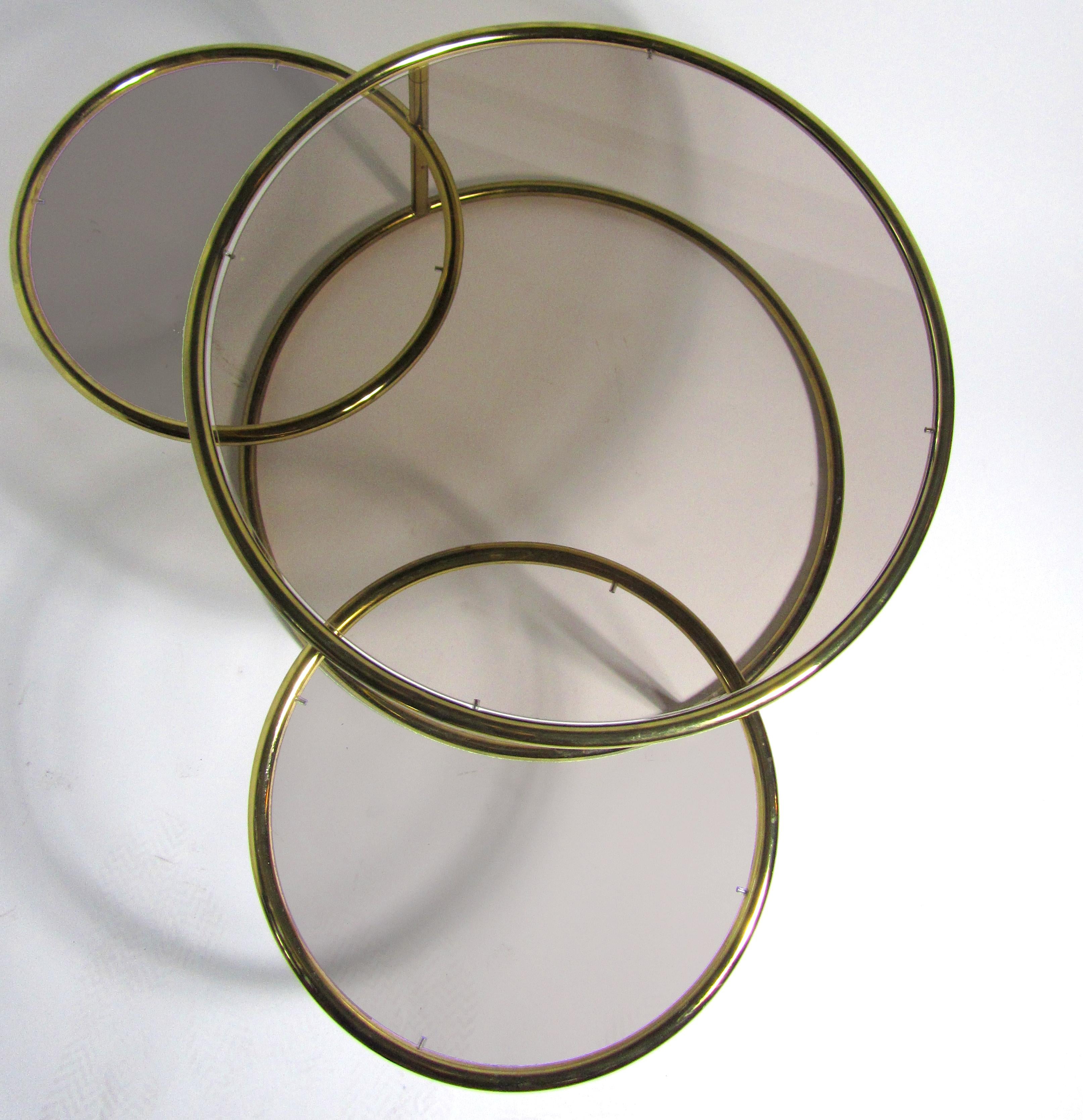 American modern brass and smoked glass three-ring coffee table by Milo Baughman. This versatile table can fold to take up a very small footprint. The table jacknife opens to have three rings exposed for additional surfaces area.