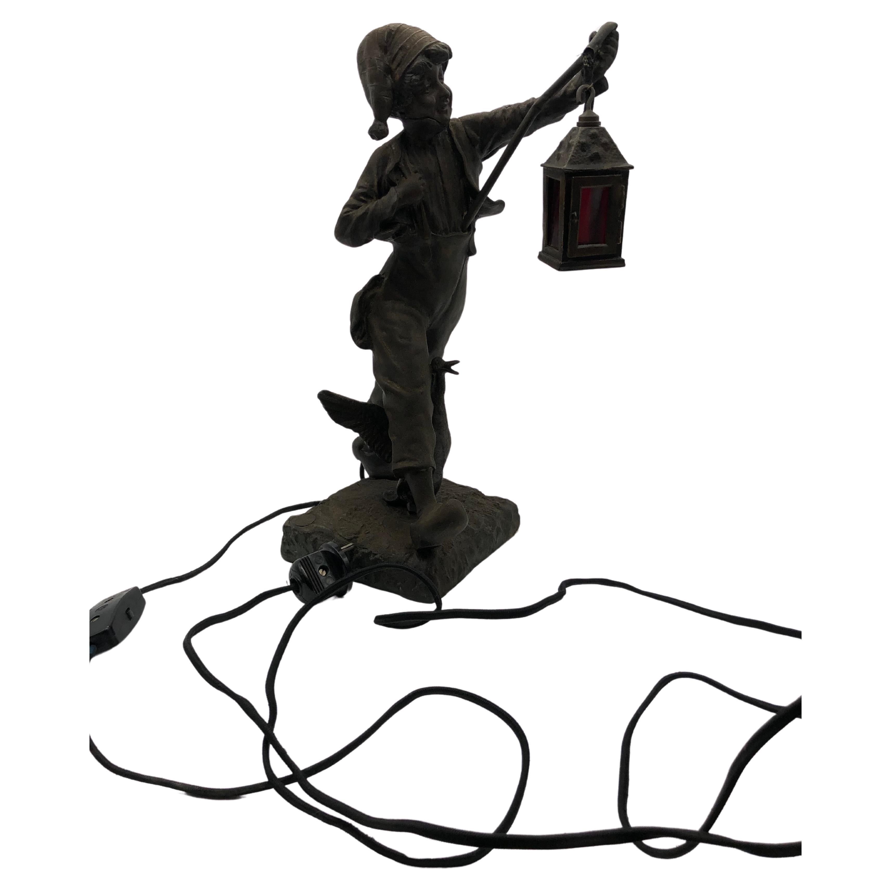 Contempla la encantadora belleza de una majestuosa figura/lámpara metálica, que desprende el encanto del bronce envejecido(Optik). Esta exquisita pieza representa a un joven, vestido con traje de dormir, acompañado de un farol, paseando junto a una