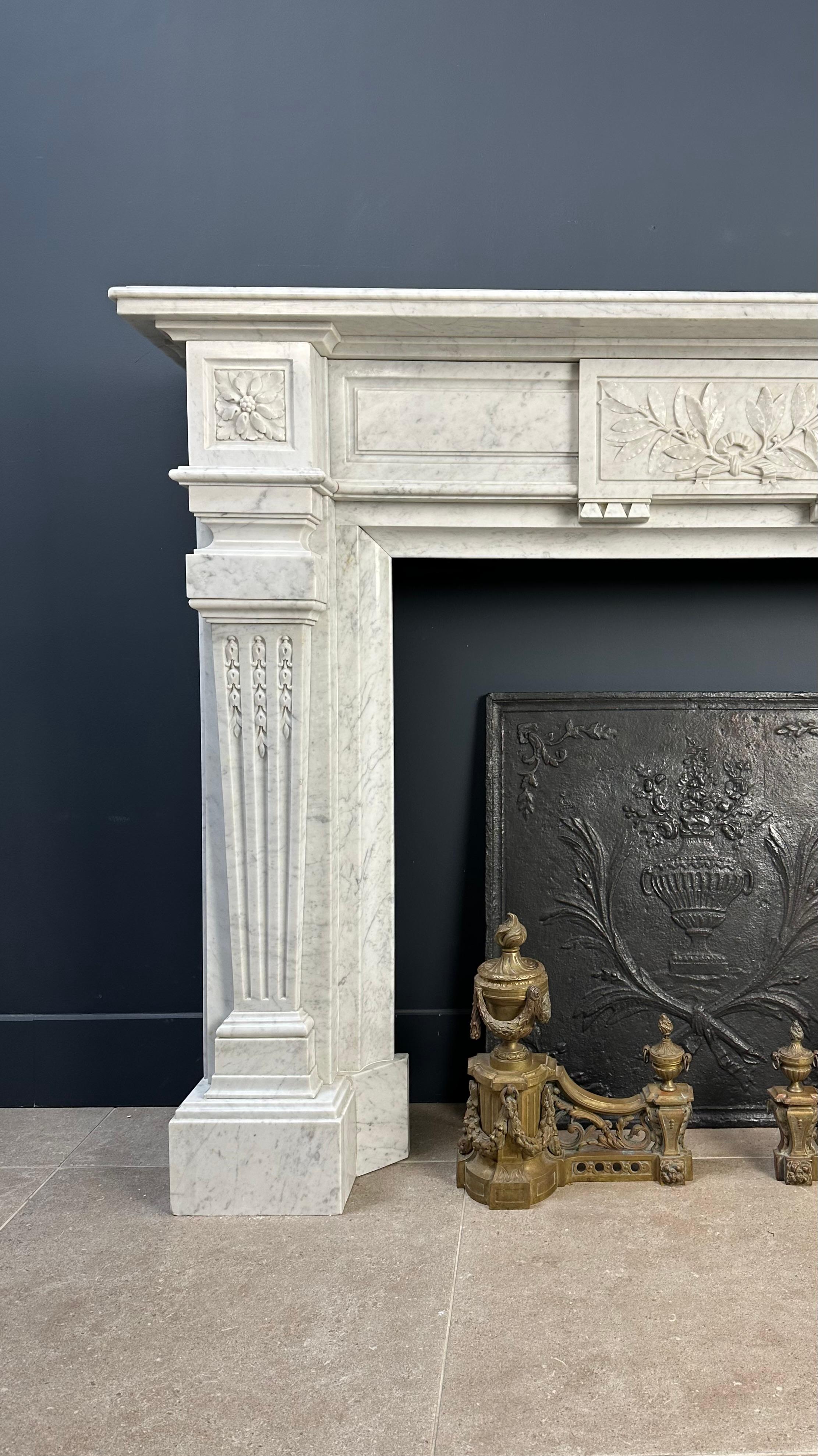 Beautiful Carrara Marble Antique Front Chimney in Empire Style. This antique fireplace boasts a commanding presence, characterized by the grandeur of the Empire style. Elaborate decorations adorn every facet of the fireplace, with the flower