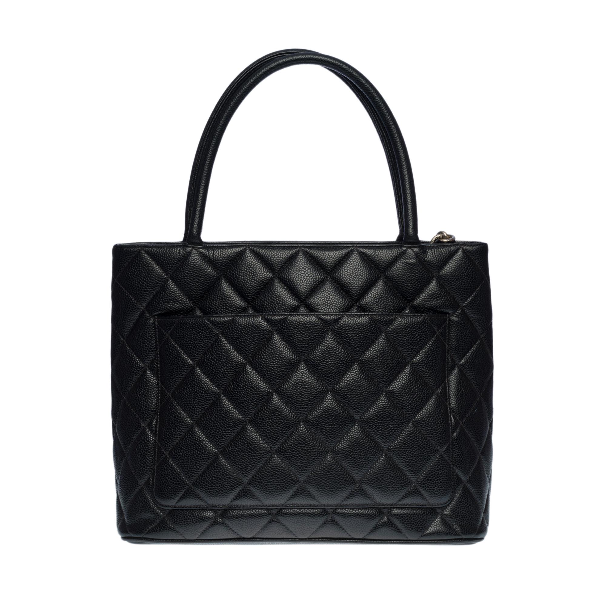 El bolso Chanel Cabas Médaillon de piel de caviar negra, herrajes de metal rutenio gris, doble asa de piel de caviar negra que permite llevarlo en la mano y al hombro

Bolsillo en la parte trasera de la bolsa
Cierre de cremallera adornado con un
