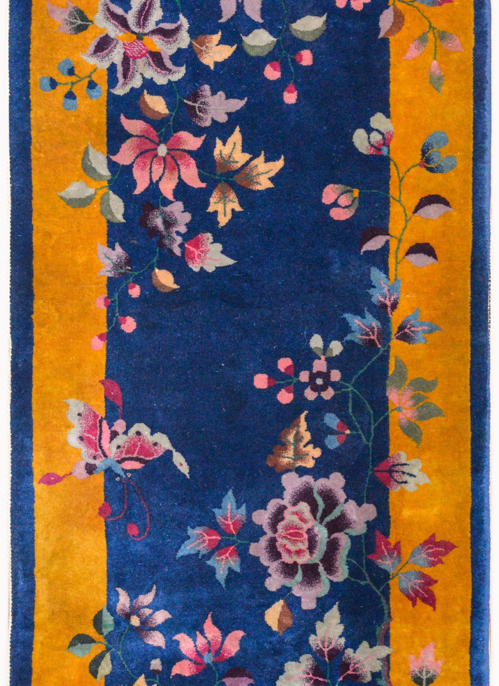 A beautiful Chinese Art Deco rug with a dark indigo field surrounded by a wide gold border. Multicolored peonies, chrysanthemum and cherry blossoms emerge from opposite corners and nearly cover the field.
