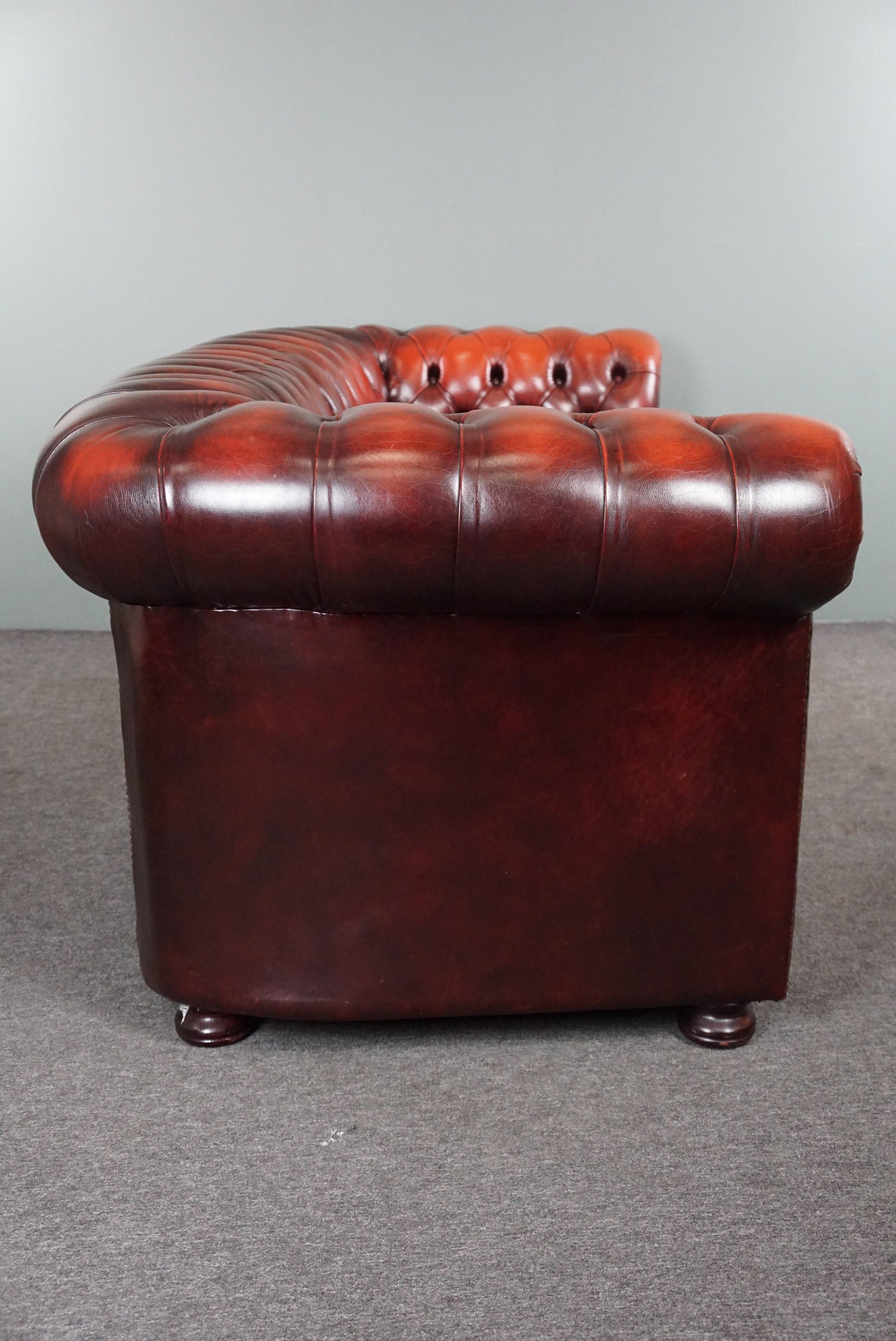 Angeboten wird dieses wunderbar sitzende, lebhaft gefärbte 2,5/3-sitzige Chesterfield-Sofa aus Rindsleder.

Dieses tiefrote Chesterfield-Sofa hat eine gepolsterte Rückenlehne und Armlehnen und ist mit Ziernägeln verziert, was ihm ein zeitloses