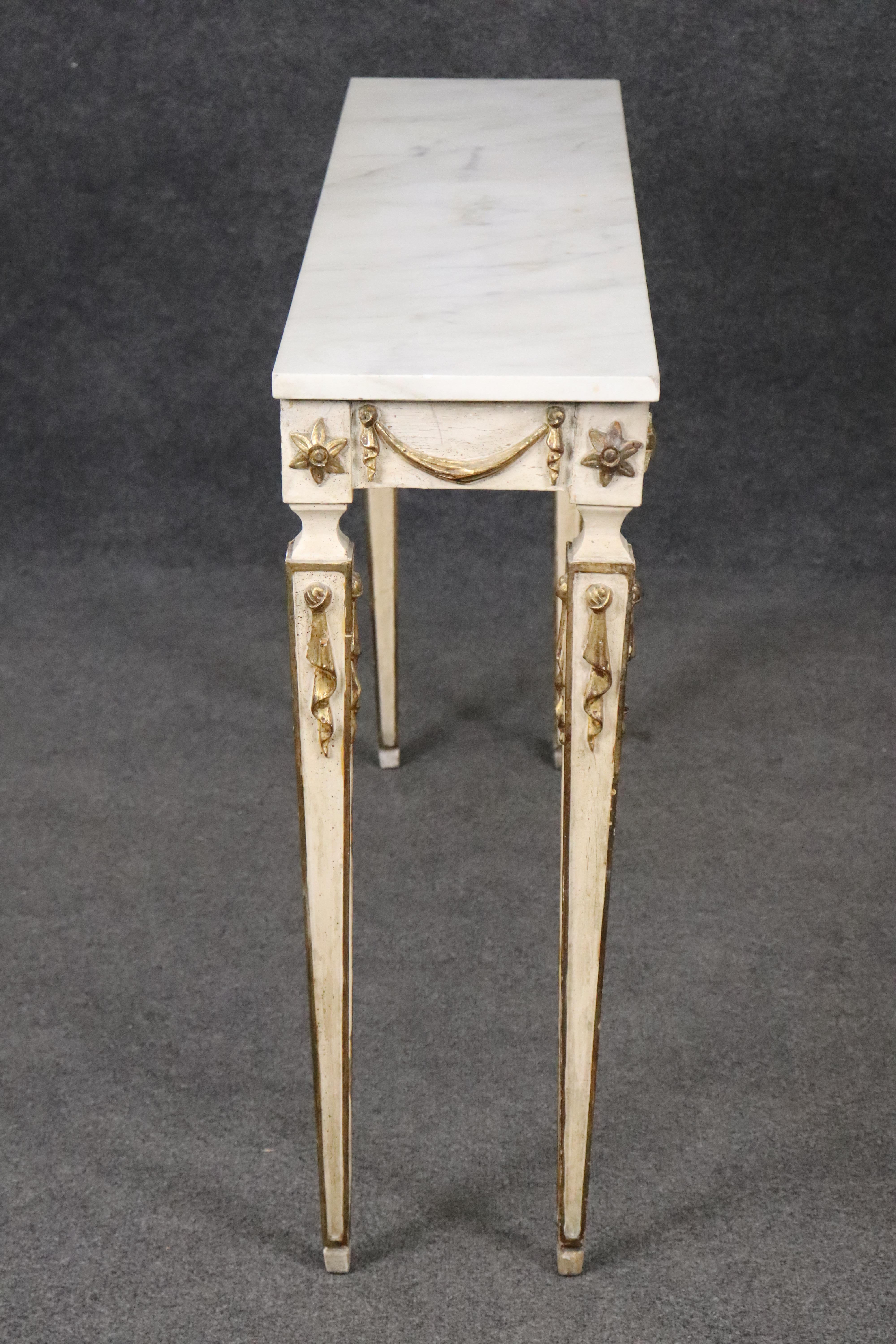 
This is a narrow, easy to place Italian-made 1950s era console. The table features a minimalist style with a creme painted background and gold leaf swags and florettes. The Carrara marble is in good condition and the table as a whole and will show