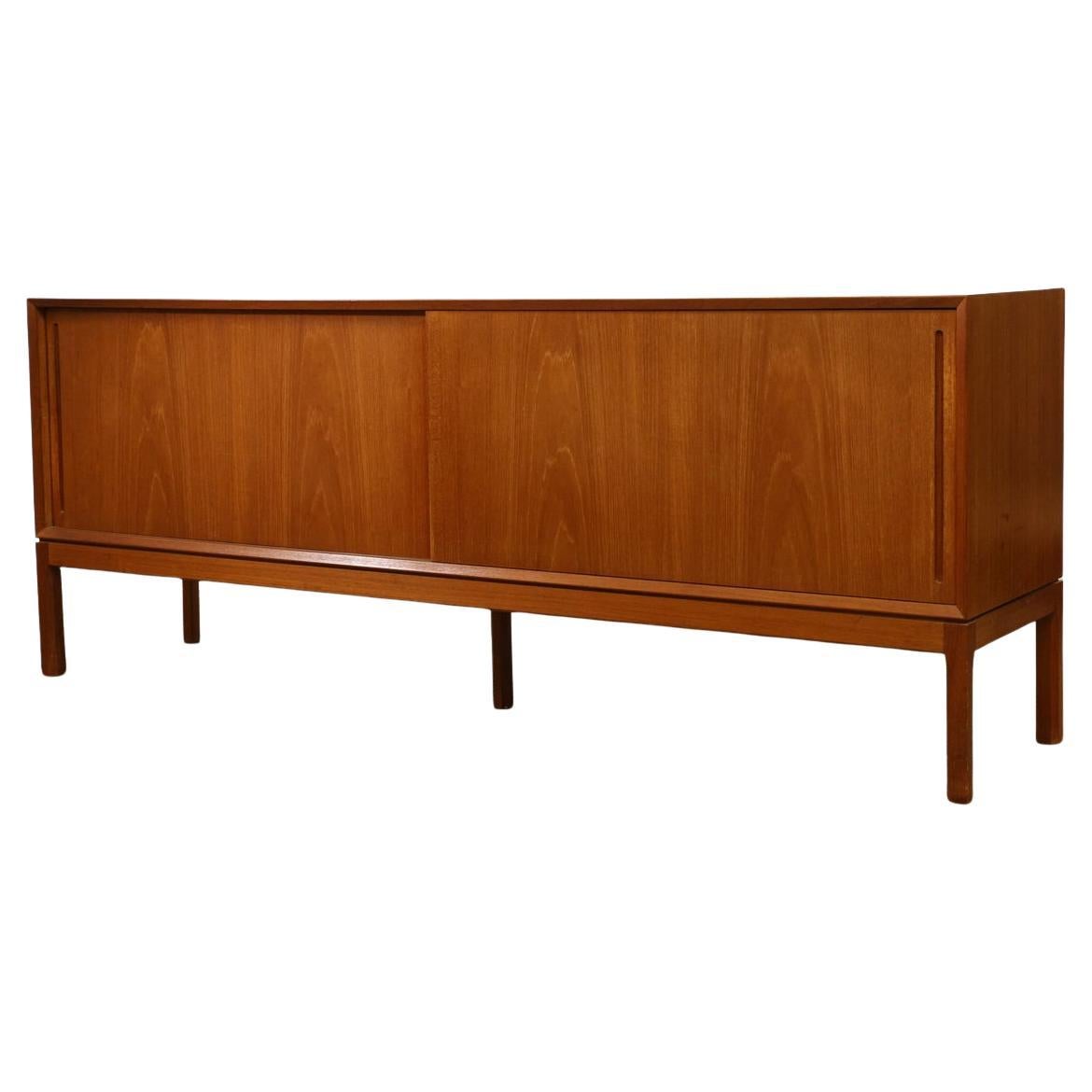 Beautiful Danish Modern teak sideboard with sliding doors with vertical concave pulls. Designed by Aksel Kjersgaard. The sliding doors open to three cabinet spaces with adjustable shelving and two drawers. The credenza sits on (5) hex shaped