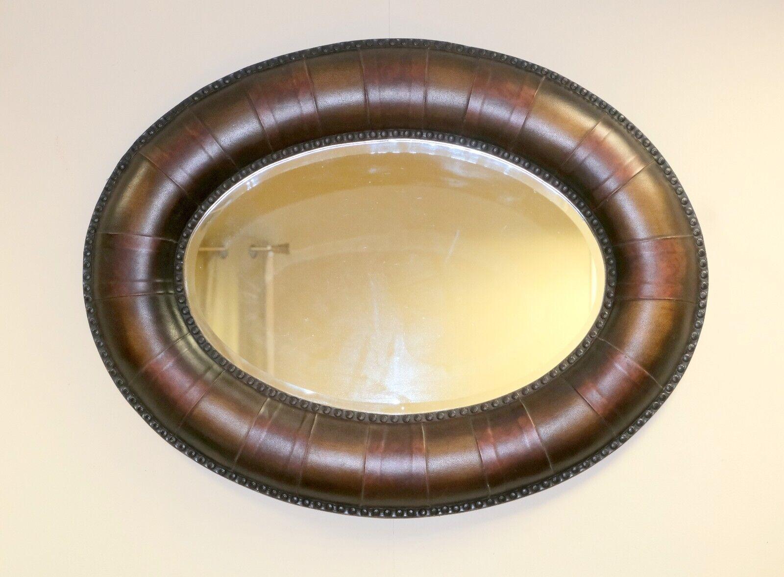 We are delighted to offer for sale this lovely, brown leather, framed, oval wall mirror with studs all around. 

This gorgeous piece will reflect the style to any room and to your walls. The cushion frame is made up of brown leather supported with
