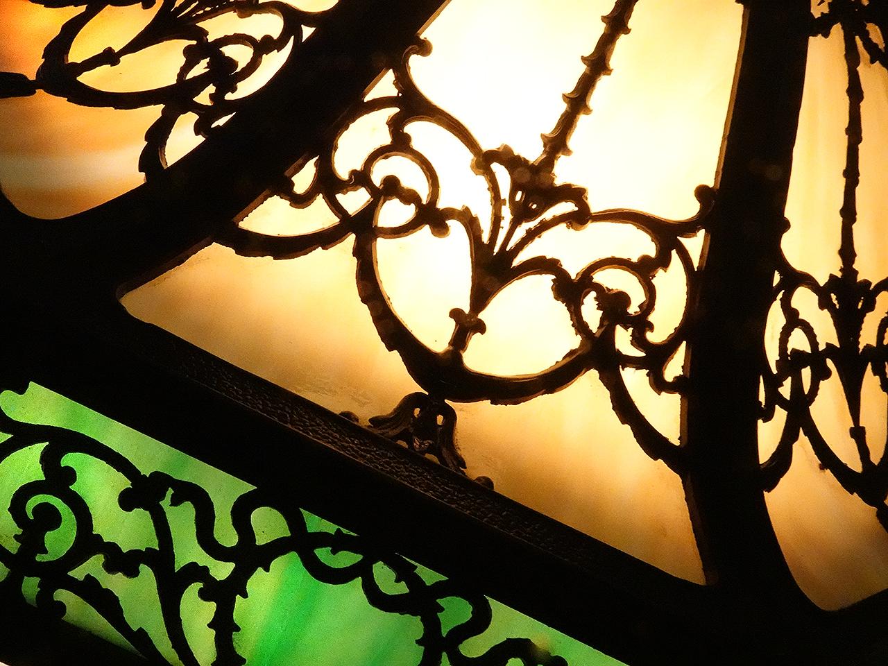 This is a large showy stained glass Victorian style table lamp. It has 8 curved and draped amber glass panels. In addition there are 8 lower contrasting emerald glass side panels. The filigree overlays cover all 16 panels. It is lit by two E26 bulb.