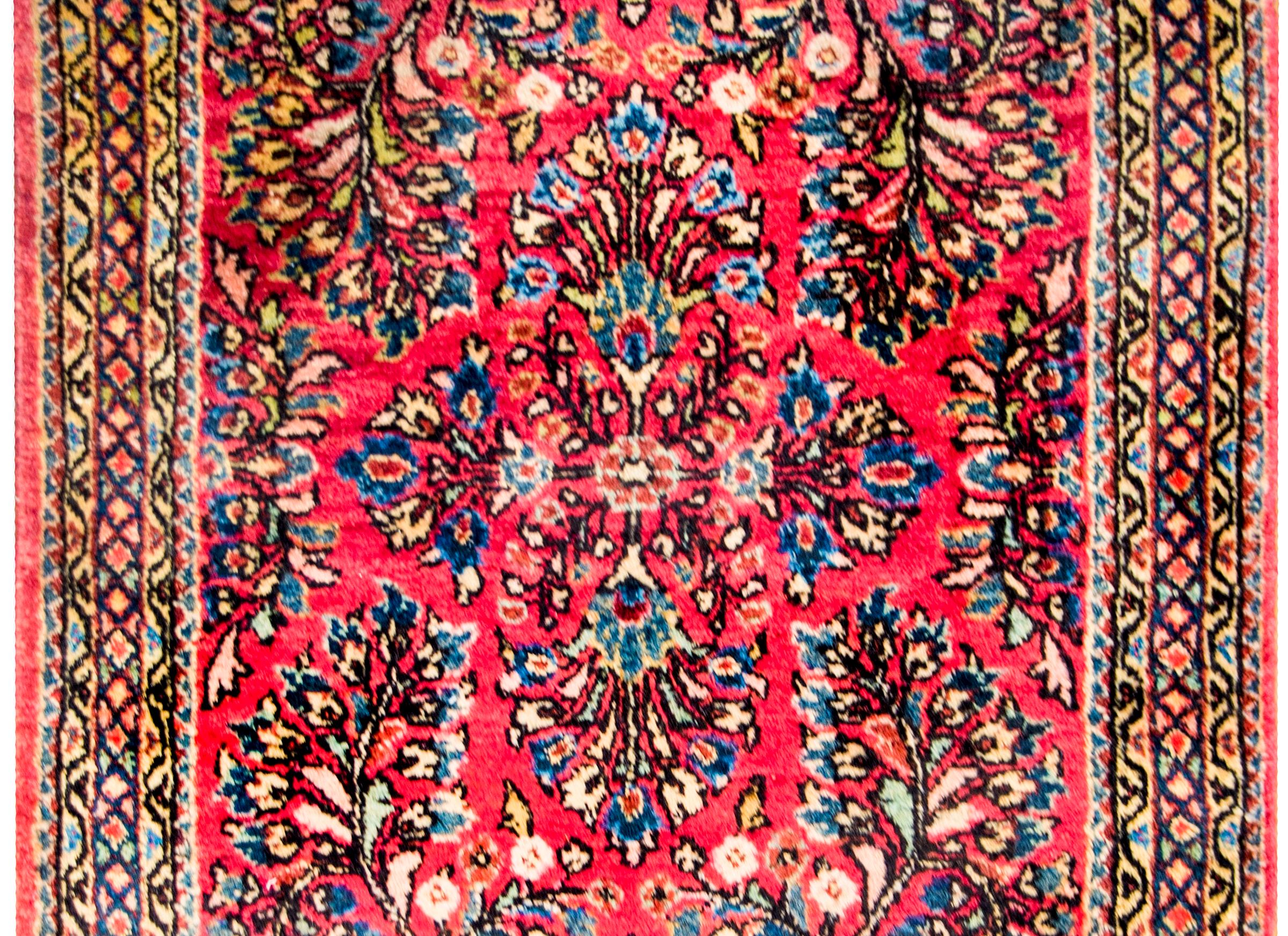 A beautiful early 20th century Persian Sarouk rug with a fantastic mirrored floral and vine pattern, expertly rendered, in light and dark indigo, gold, and brown, on a bold cranberry background. The border is wide, with multiple petite floral