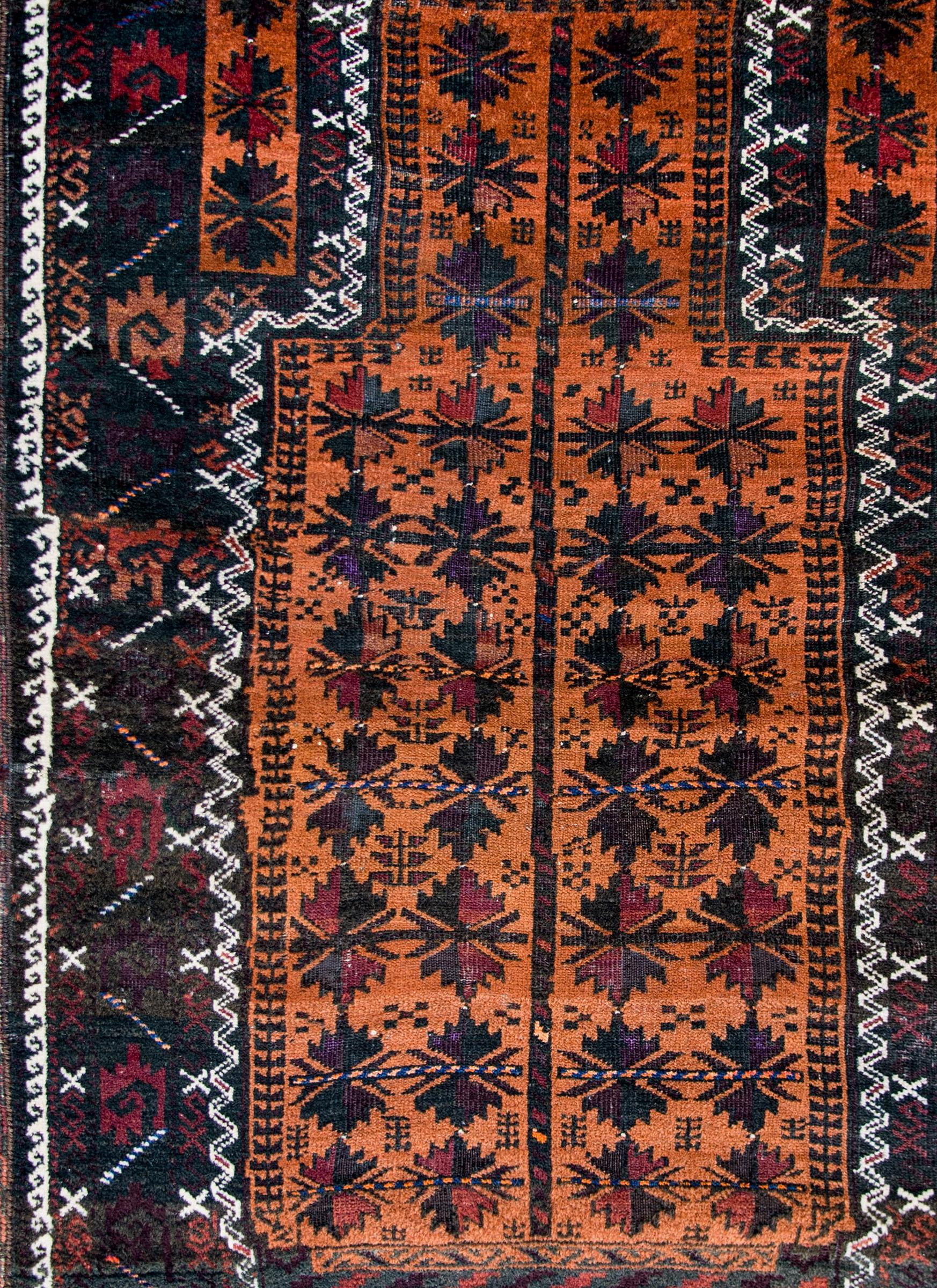 An early 20th century Persian Baluch prayer rug with an all-over floral pattern woven in black and deep cranberry colored wool on an orange background surrounded by a complementary stylized floral border women in similar colors.