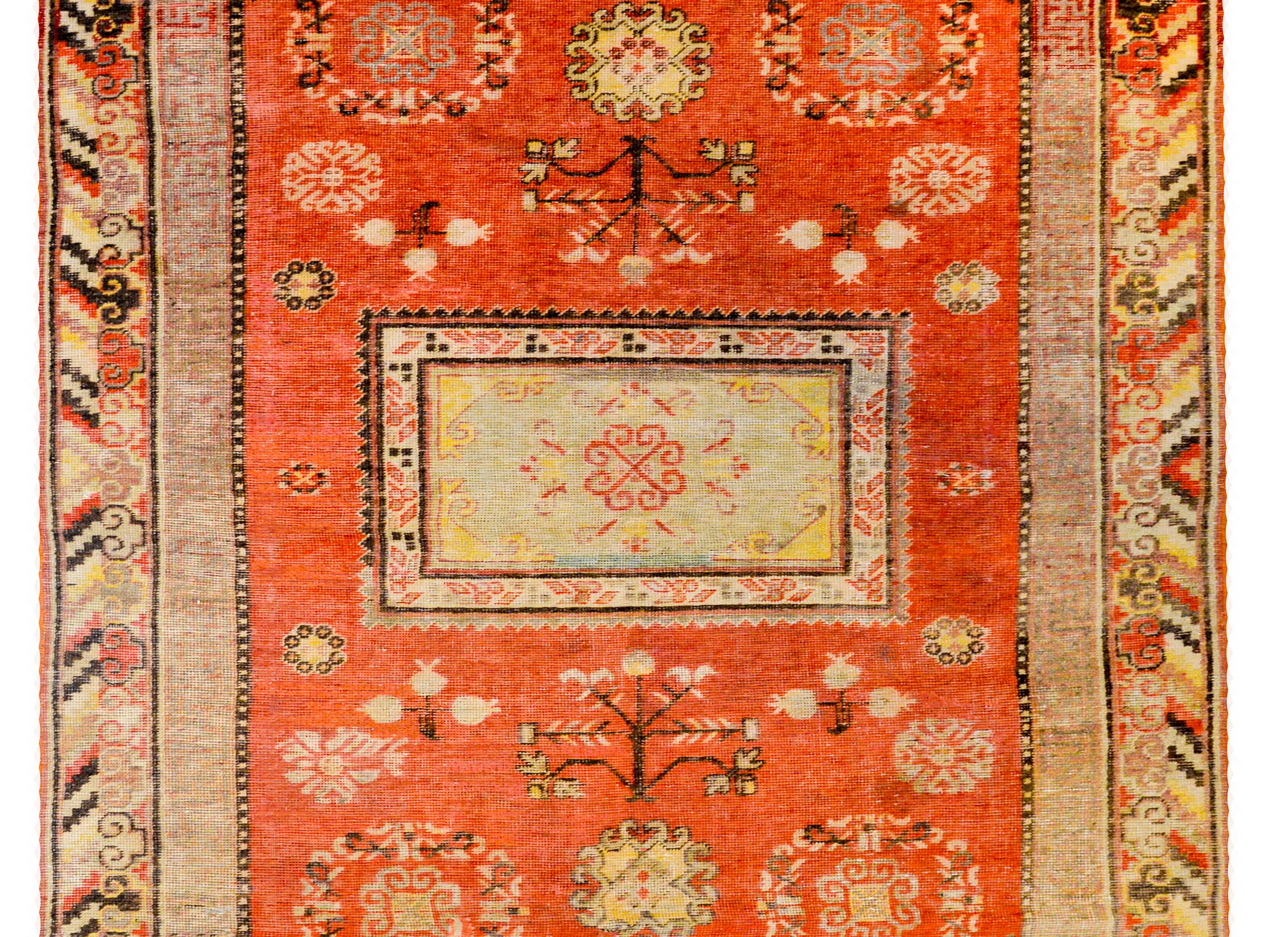 A beautiful early 20th century Central Asian Khotan rug with a large square medallion amidst a field of flowering trees-of-life, pomegranates, and stylized flowers, on a bright crimson field. The border is complementary with an inner meandering