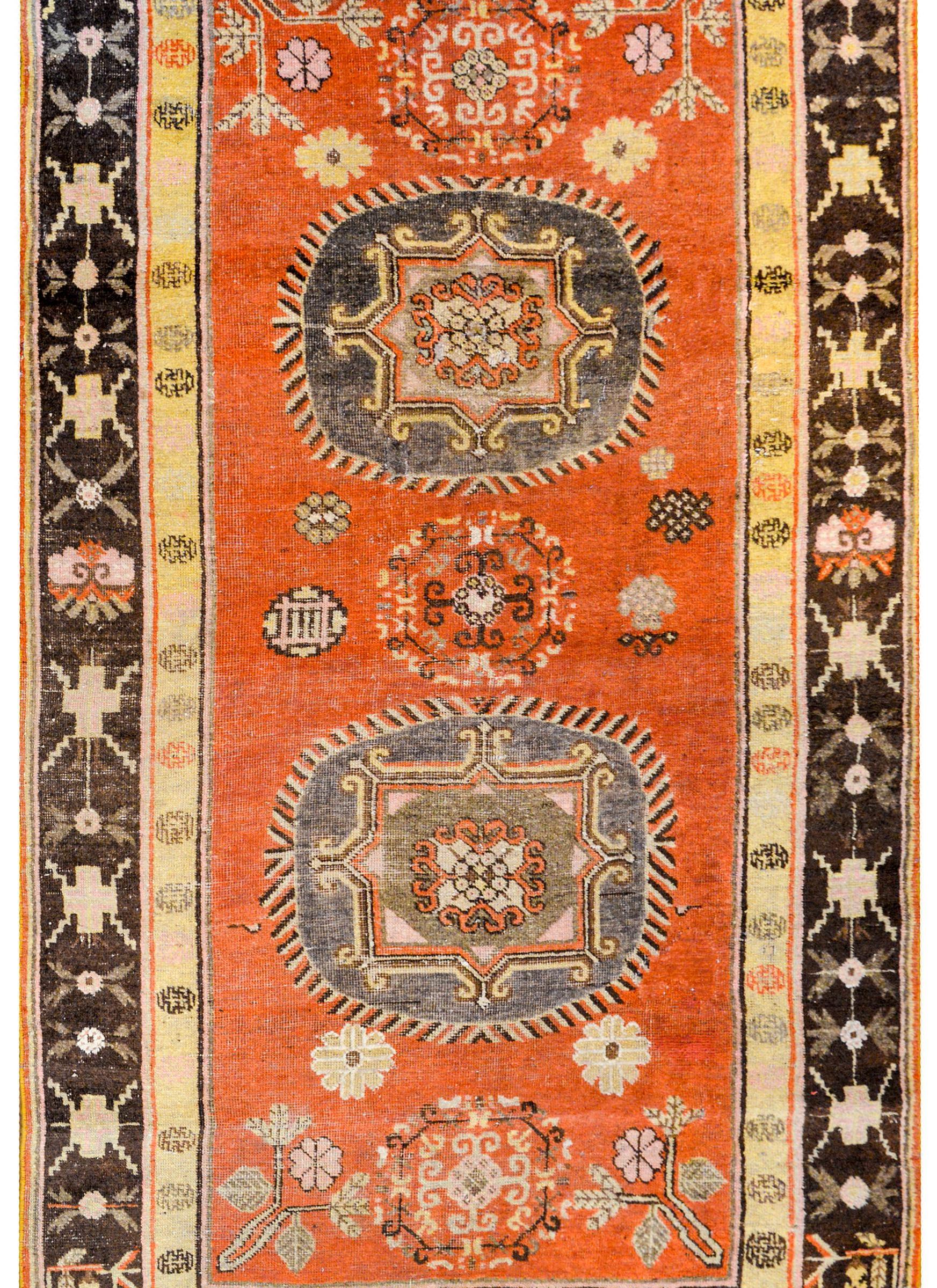 A wonderful early 20th century central Asian Samarghand rug with two large circular medallions woven in muted lavender on a bold orange field of peonies and other stylized flowers, surrounded by a beautiful brown border with more stylized flowers