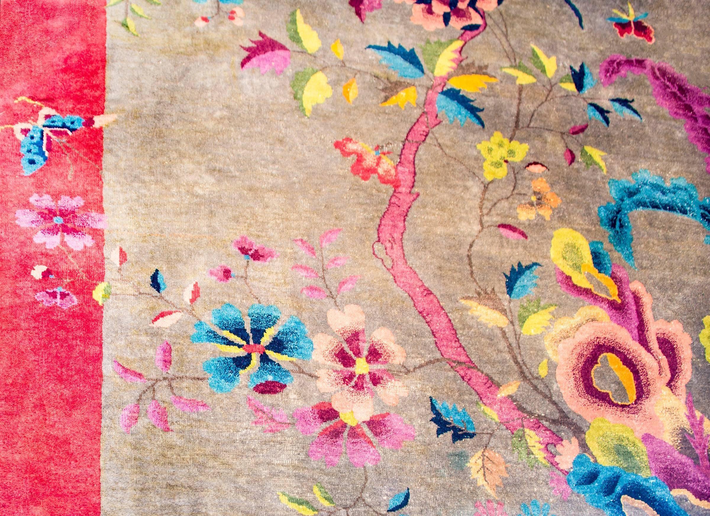 A beautiful early 20th century Chinese Art Deco rug with a fantastic pattern containing an asymmetrical multicolored flowering tree peony growing from the base of a scholar's rock with a phoenix and magpie in flight, on a grey background, surrounded