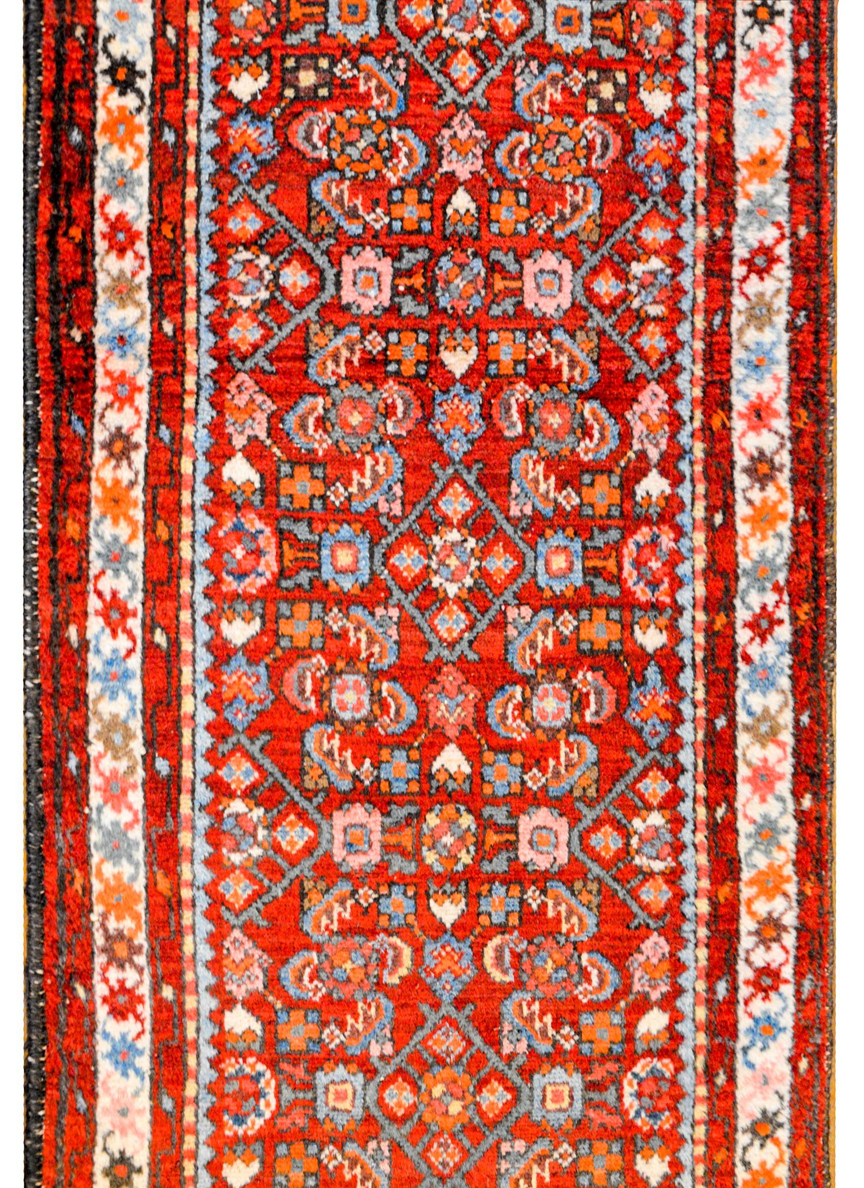 A beautiful early 20th century Persian Dargazin Herati runner with a fantastic all-over trellis and floral pattern woven in orange, cream, light indigo, and grey colored wool on a bright crimson background, surrounded by a multiple petite stylized