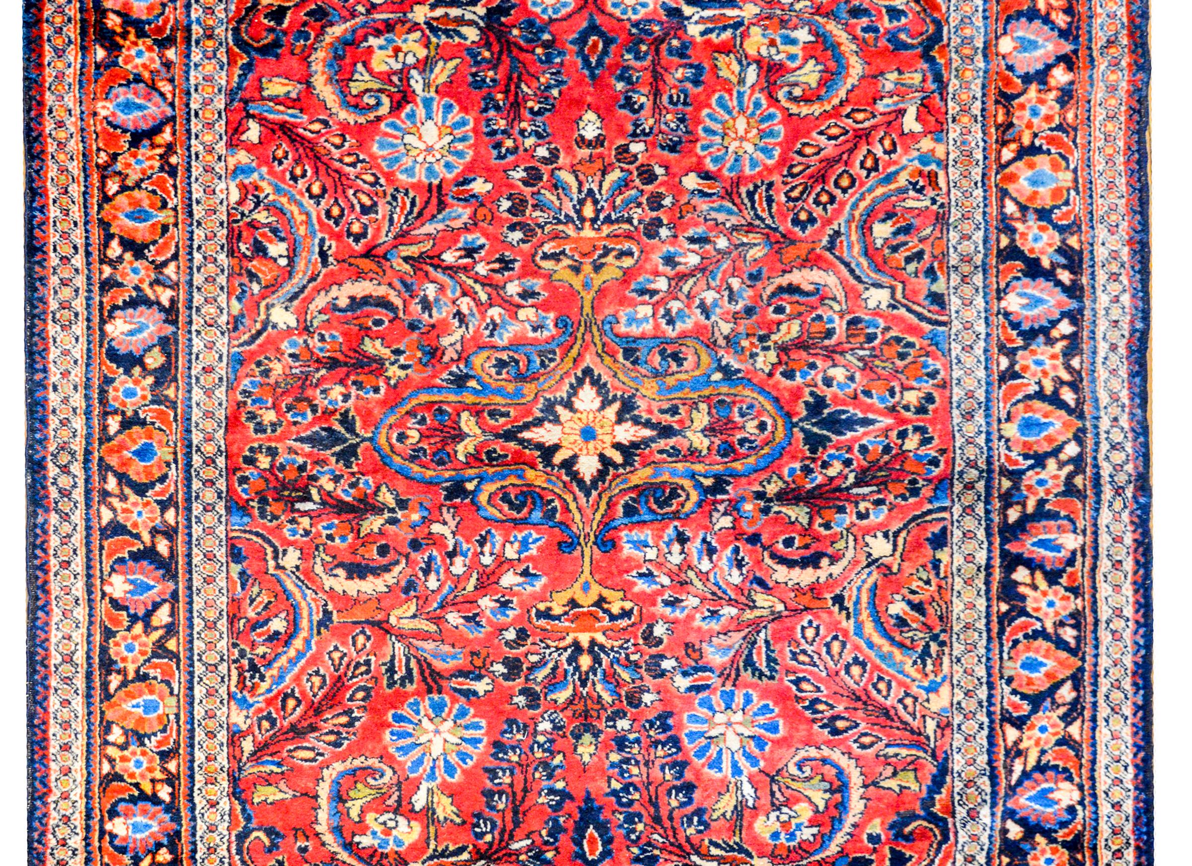 A beautiful early 20th century Persian Lilihan rug with a large-scale mirrored floral patterned field woven in light and dark indigo, pink, gold, and cream colored wool on a rich cranberry field, surrounded by a wonderful border containing a wide