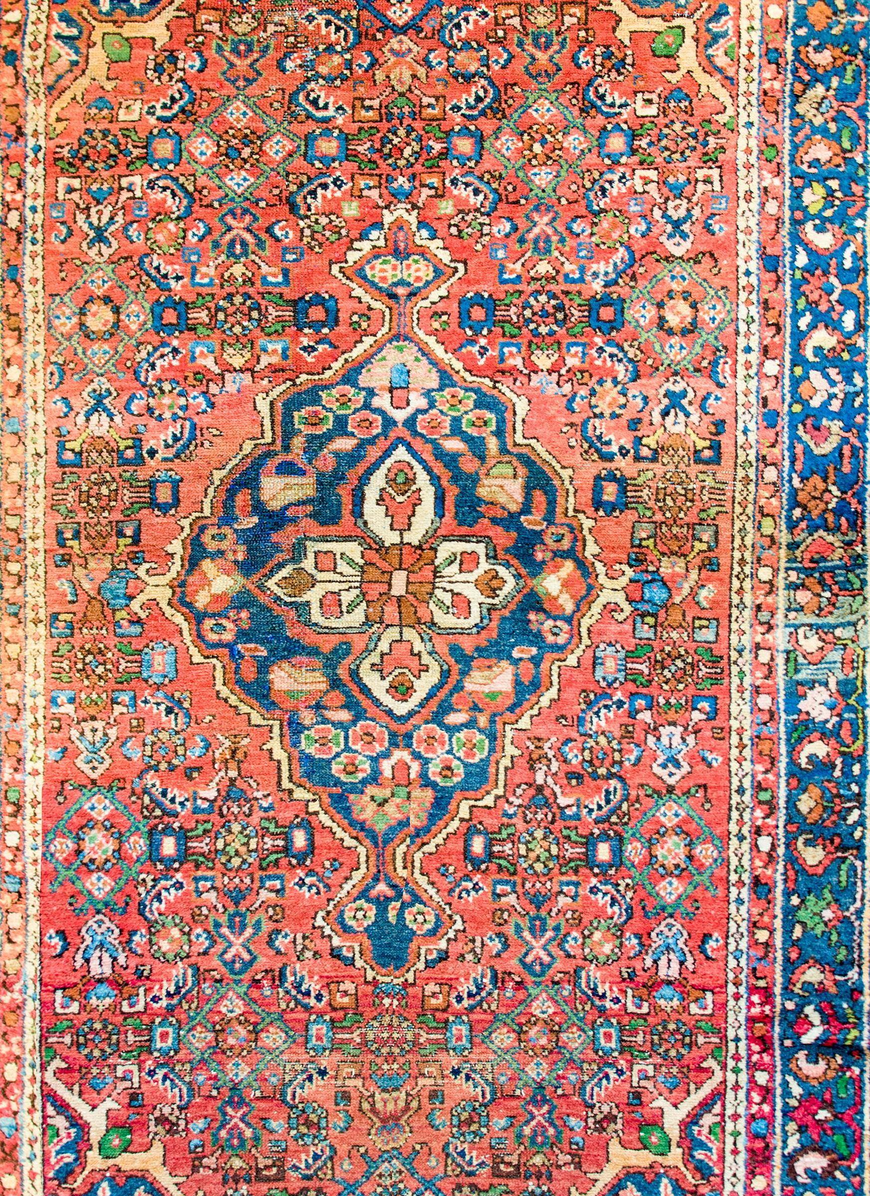 A beautiful early 20th century Persian Malayer rug with a large central diamond floral medallion with myriad flowers woven in crimson, indigo, green, gold, and black vegetable dyed wool on a crimsons field of additional myriad flowers. The border is