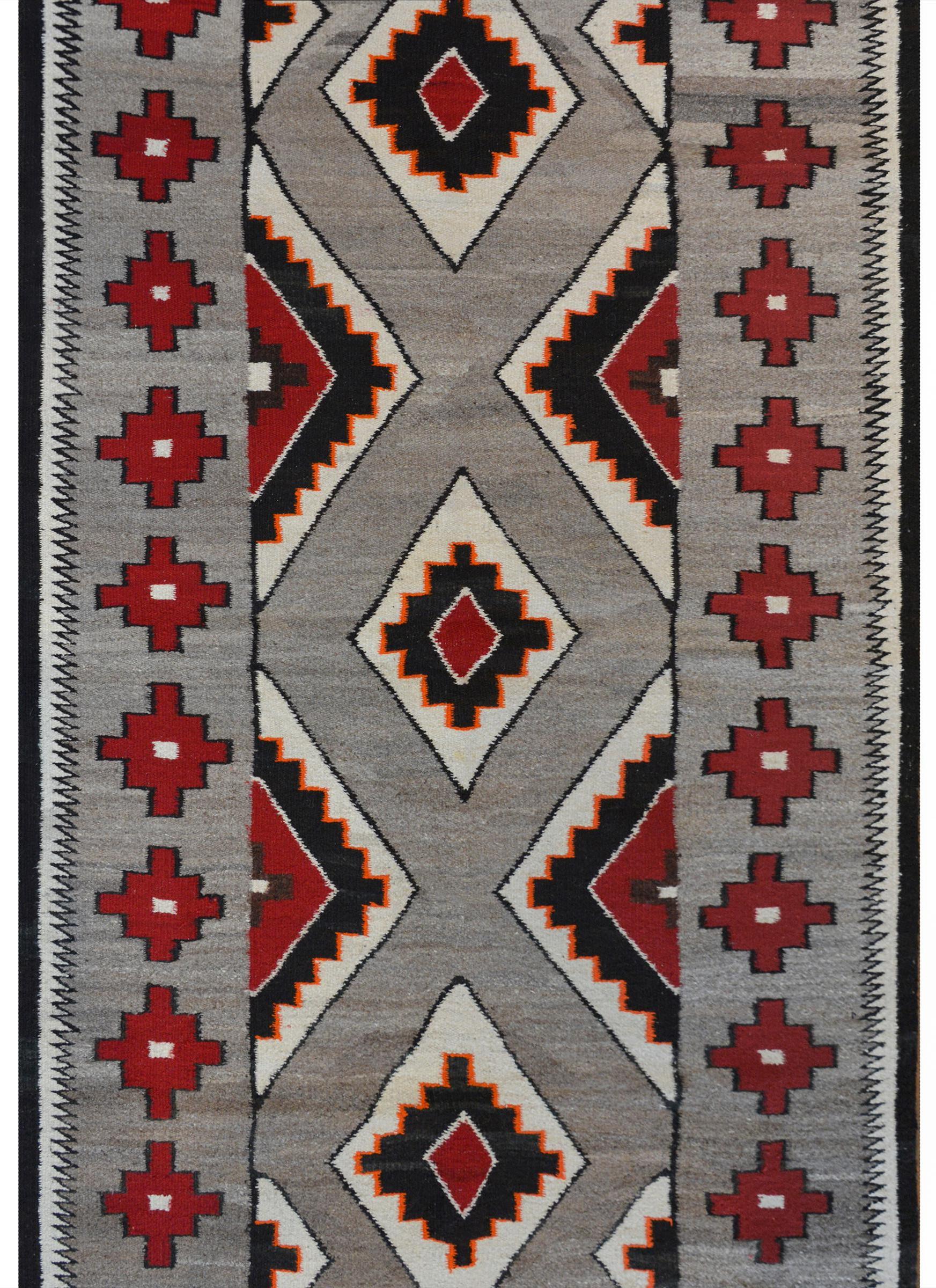 A beautiful early 20th century Navajo rug with a wonderful pattern containing multiple diamonds across the field, woven in cream, crimson, black, and orange colored wool on a gray background surrounded by a simple border of crimson diamonds.