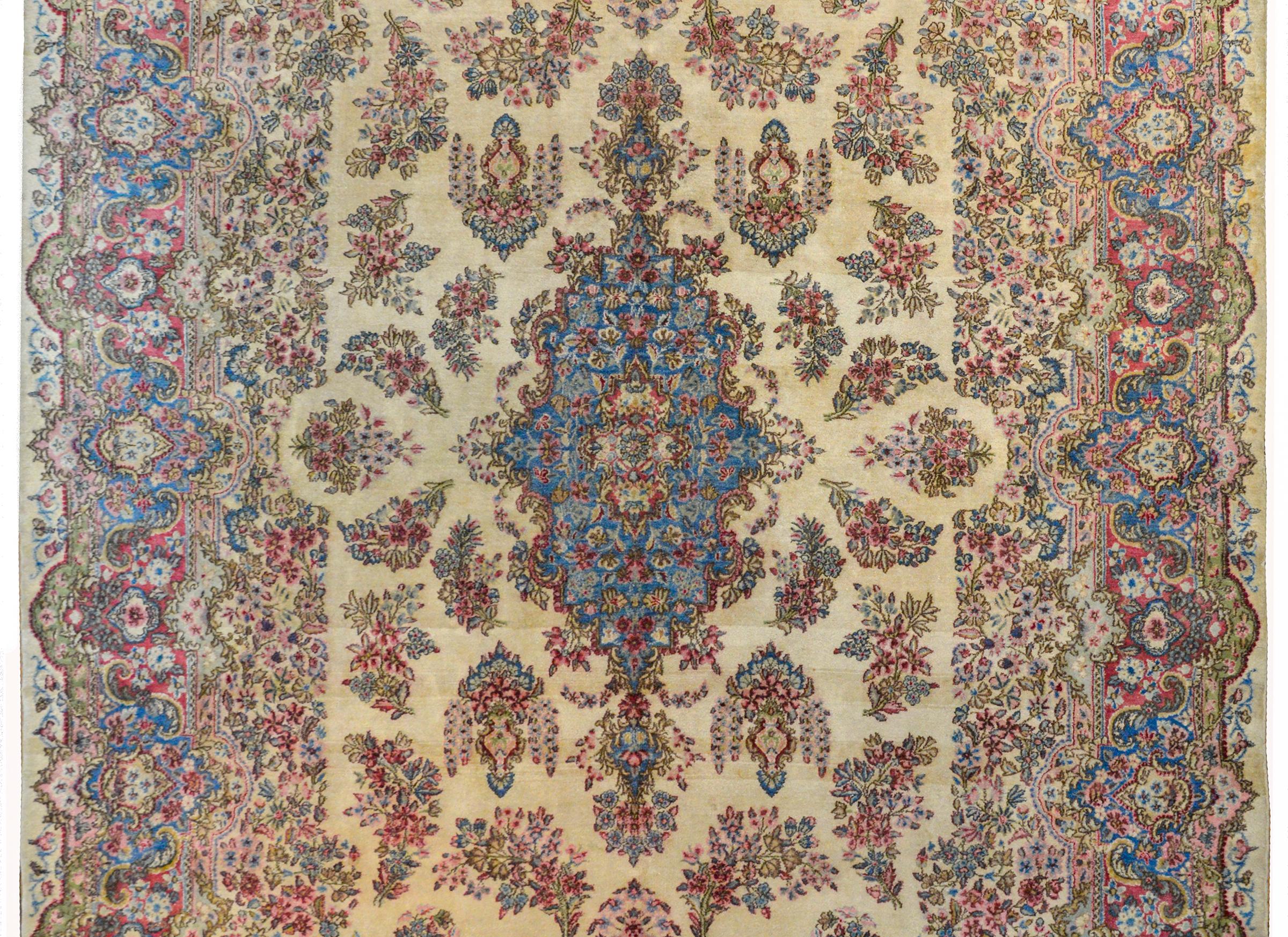 A beautiful early 20th century Persian Kirman rug with a large central indigo floral patterned medallion on a cream colored background amidst a field of more flowers. The border is extraordinary with myriad flowers woven in similar colors as the