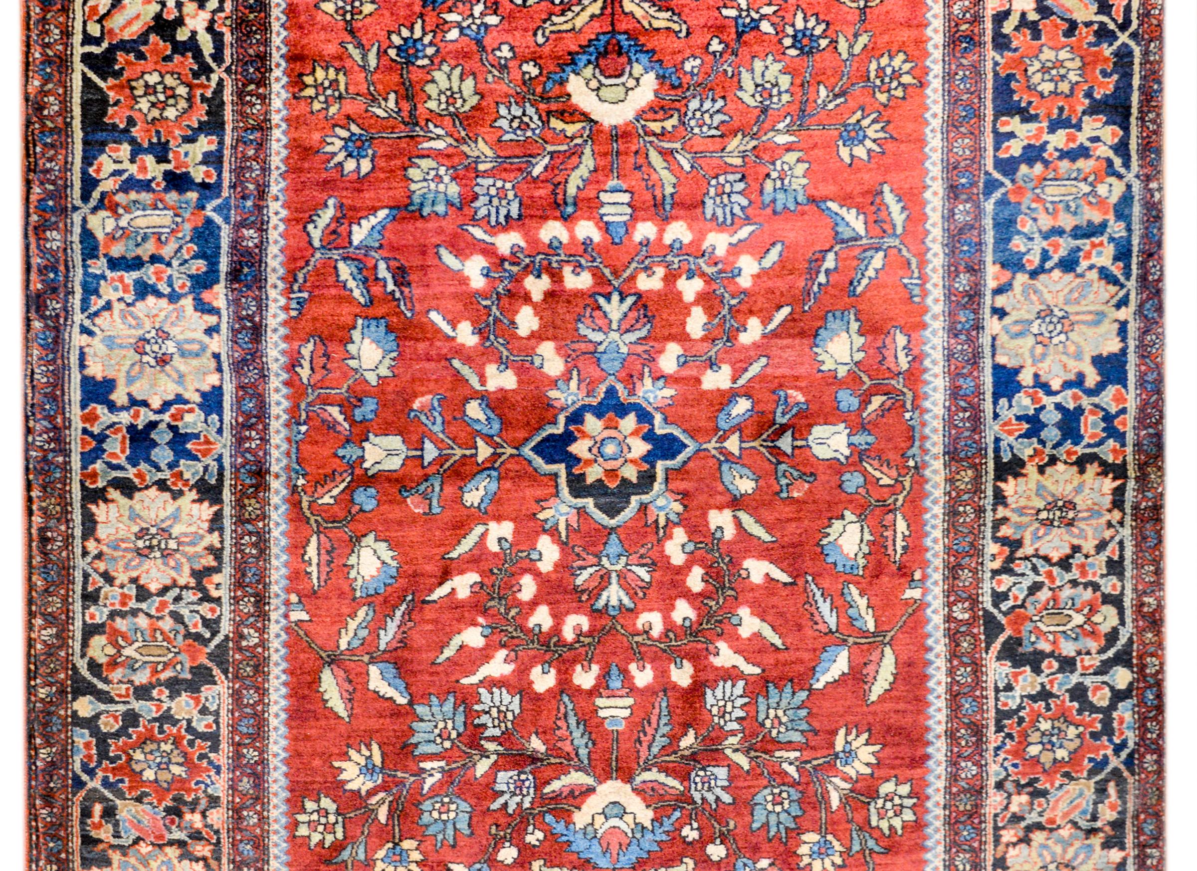 A beautiful early 20th century Persian Sarouk Farahan rug with a mirrored floral and vine pattern woven in light and dark indigo, green, and cream colored wool, in a bright crimson background. The border is elaborate with a large-scale floral and