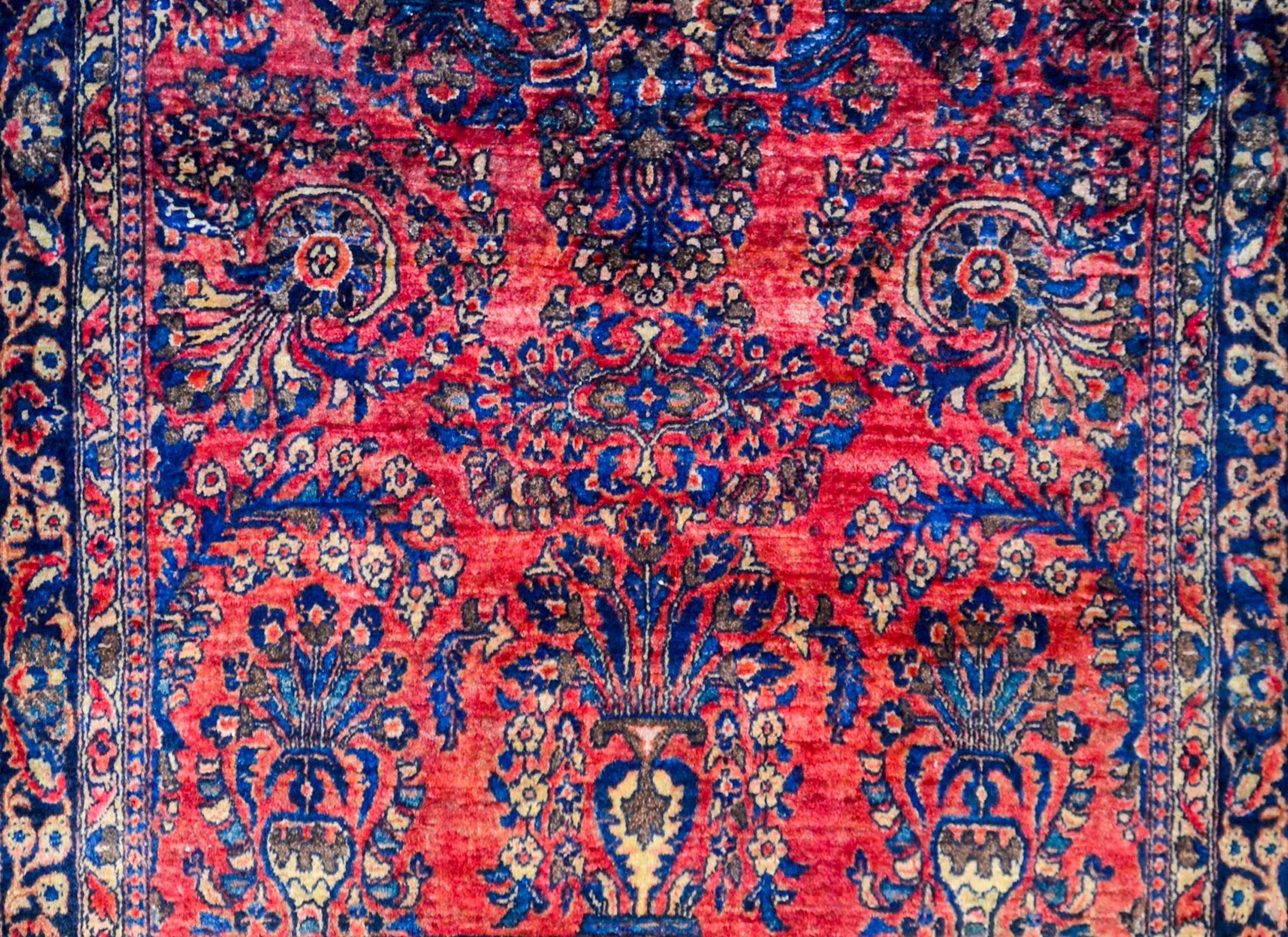 A beautiful early 20th century Persian Sarouk rug with a fantastic mirrored floral and vine pattern, expertly rendered, in light and dark indigo, pink, and natural undyed wool, on a bold cranberry background. The border is wide, with a wide stripe