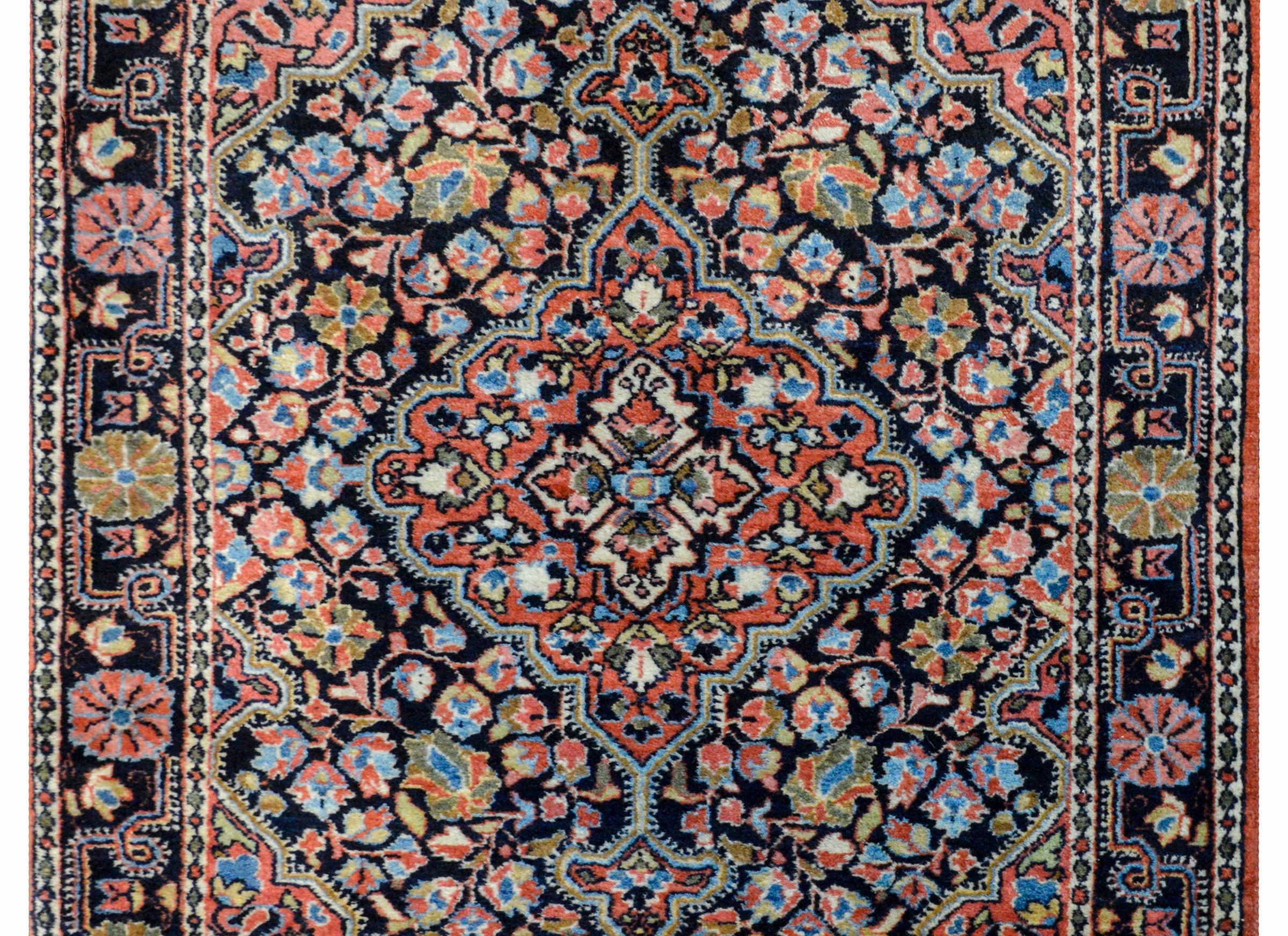 A beautiful early 20th century Persian Sarouk rug with a large central floral medallion amidst a field of flowers and scrolling vines woven in myriad colors including crimson, green, gold, white, and light and dark indigo, all on a black background,