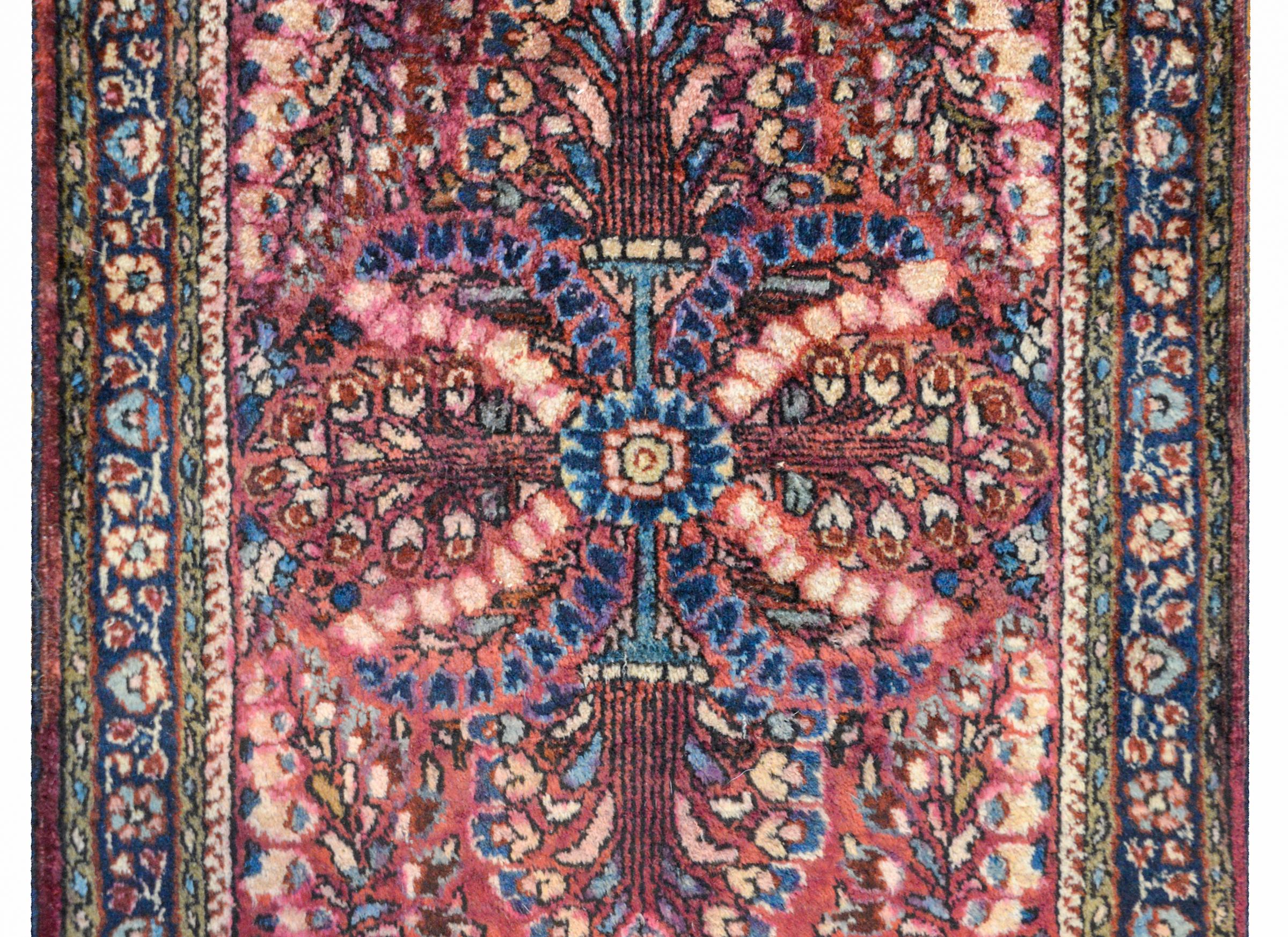 A beautiful early 20th century Persian Sarouk rug with a mirrored tree-of-life pattern woven in cream, cranberry, light and dark indigo, and pink colored vegetable dyed wool surrounded by a complex border of multiple floral patterned stripes.