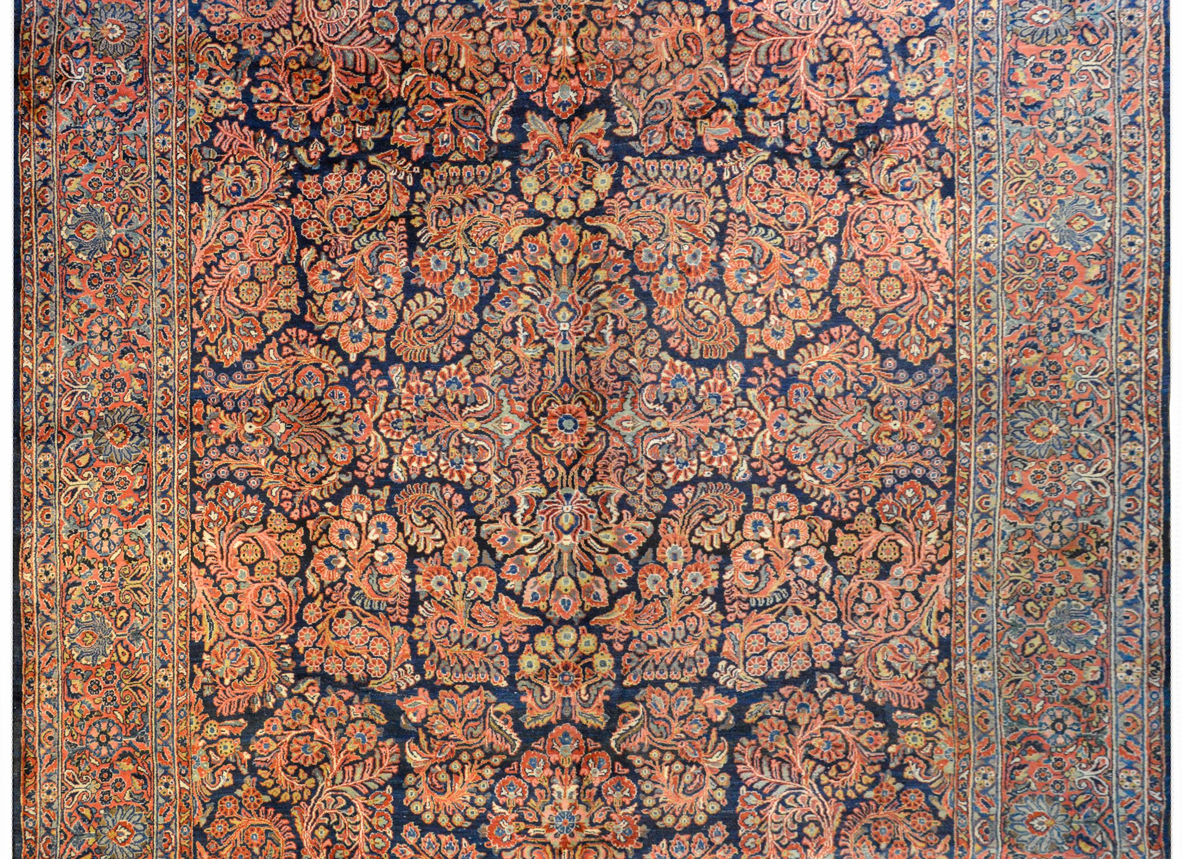 A beautiful early 20th century Persian Sarouk rug with an all-over floral cluster pattern woven in light and dark indigo, green, coral, and cream on a dark indigo background surrounded by wonderful floral patterned border with a wide central floral