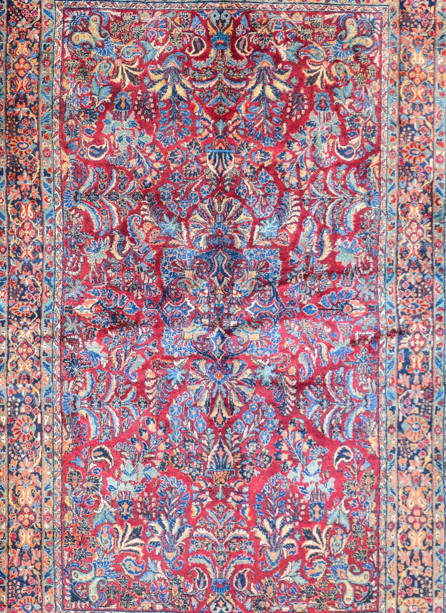A beautiful early 20th century Persian Sarouk rug with a large-scale mirrored floral pattern woven in traditional colors of light and dark indigo, cream, and pink, against a rich cranberry colored background. The border is complex with multiple
