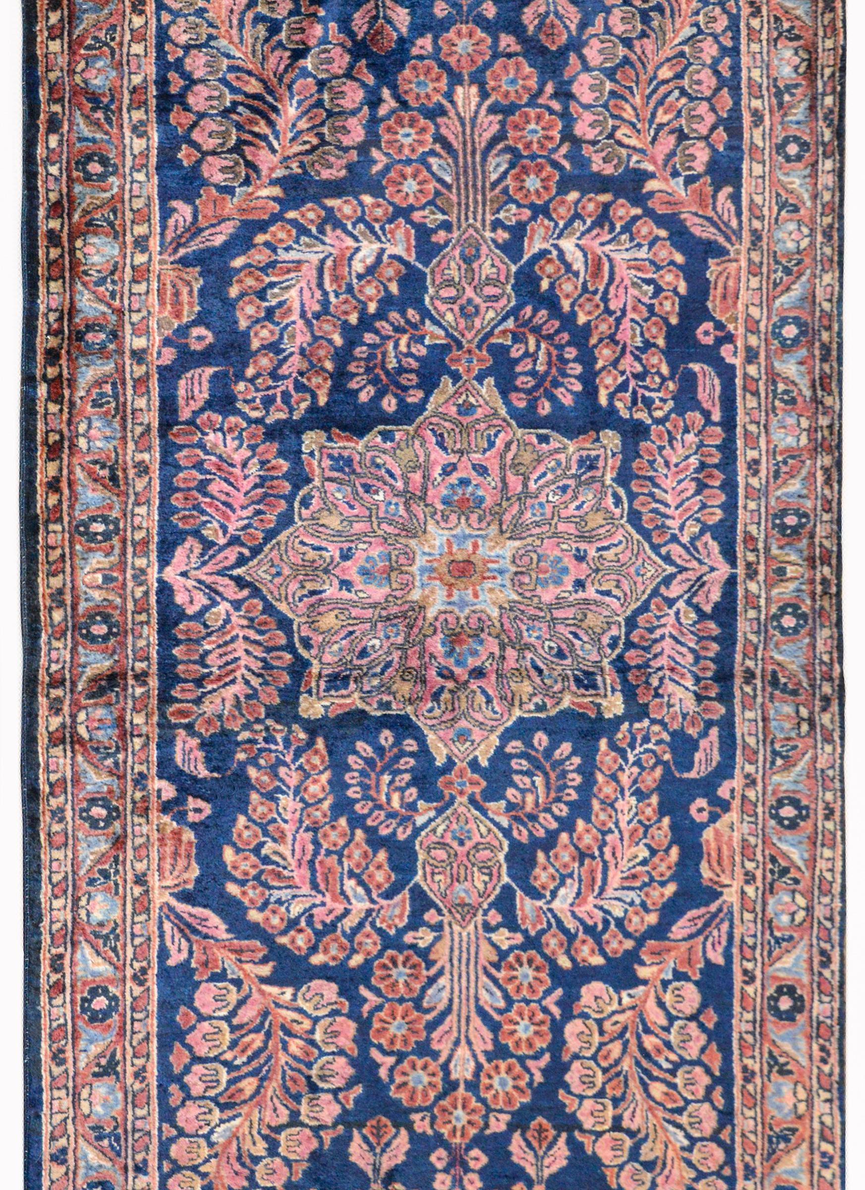 A beautiful early 20th century Persian Sarouk rug with large central floral medallion woven in myriad colors against a dark indigo background, and amidst a field or mirrored large scale scrolling vines, flowers, and leaves. The border is complex