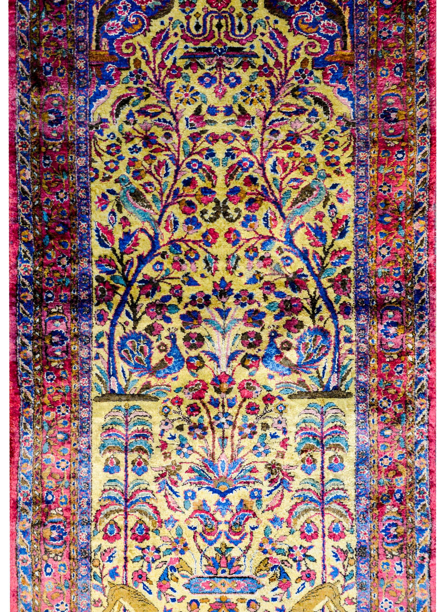 A wonderful early 20th century Persian Kashan rug woven with a large central Tree-of-Life and peacock pattern woven in light and dark indigo, crimson, pink, and green vegetable dyed 100% silk, on a brilliant gold background. The border is complex