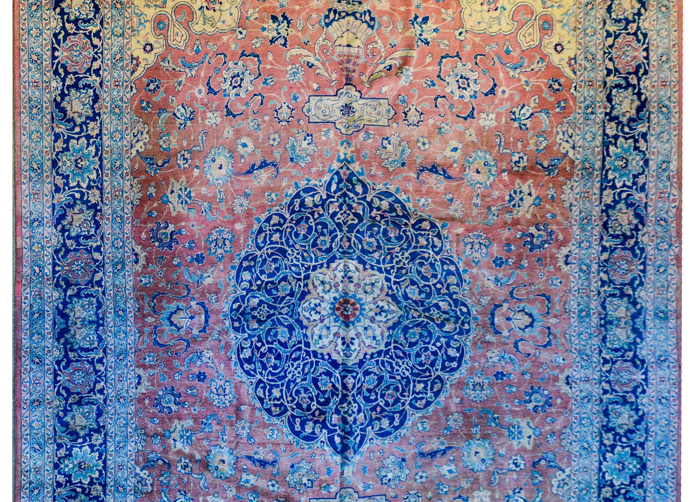 A beautiful early 20th century Persian Tabriz rug with a fantastic large central floral medallion woven in indigo, pink, and gold, on a wonderful salmon colored ground with myriad flowers and scrolling vines. The border is wide with one wide central